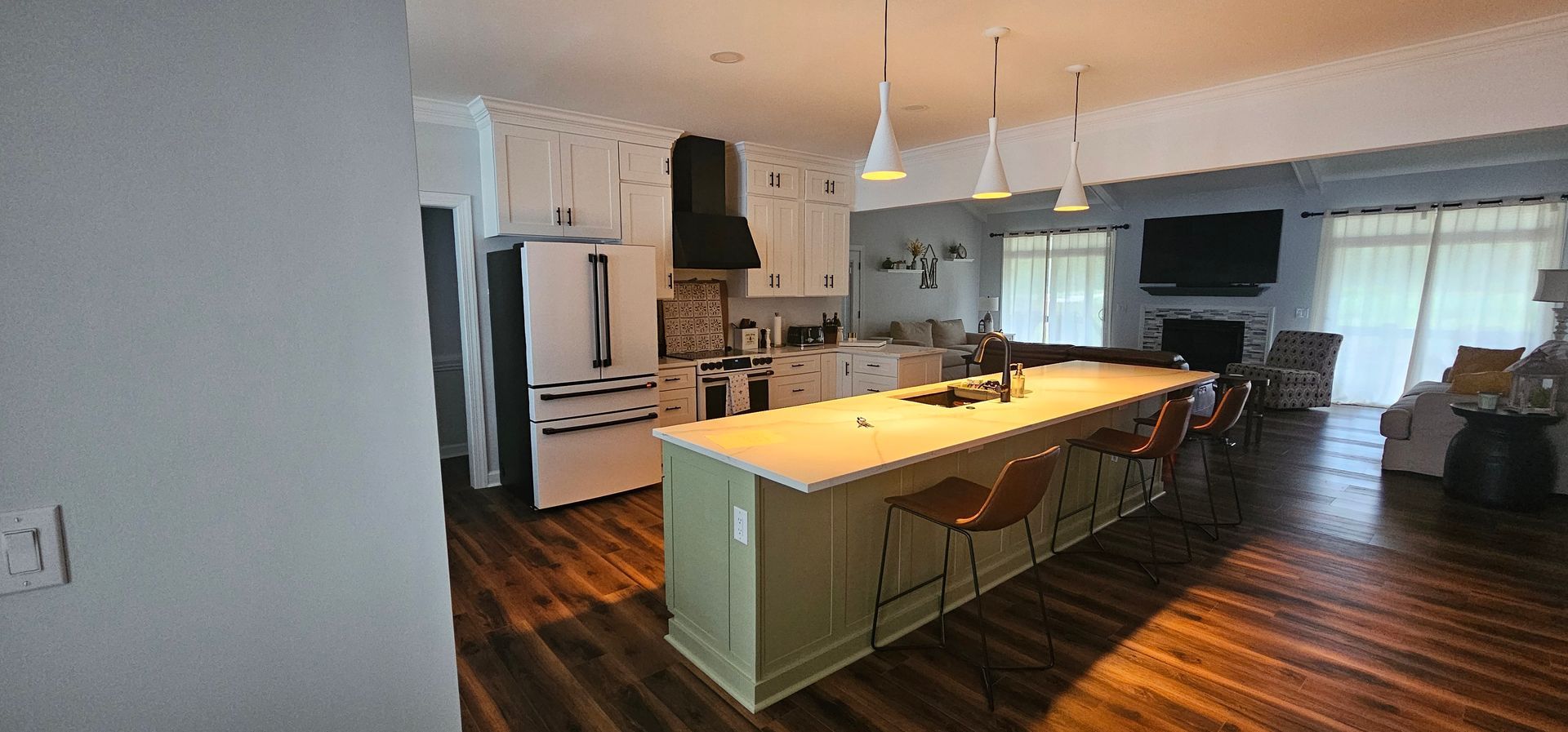 Open kitchen with a large island, white cabinets, wood floors, and pendant lights in a bright living space