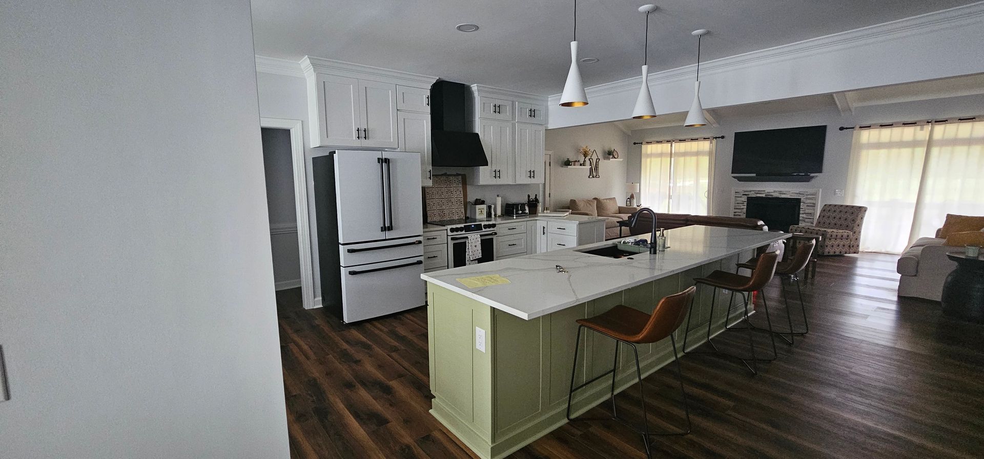 Bright open-plan kitchen with white cabinets, island seating, wood floors, and large windows