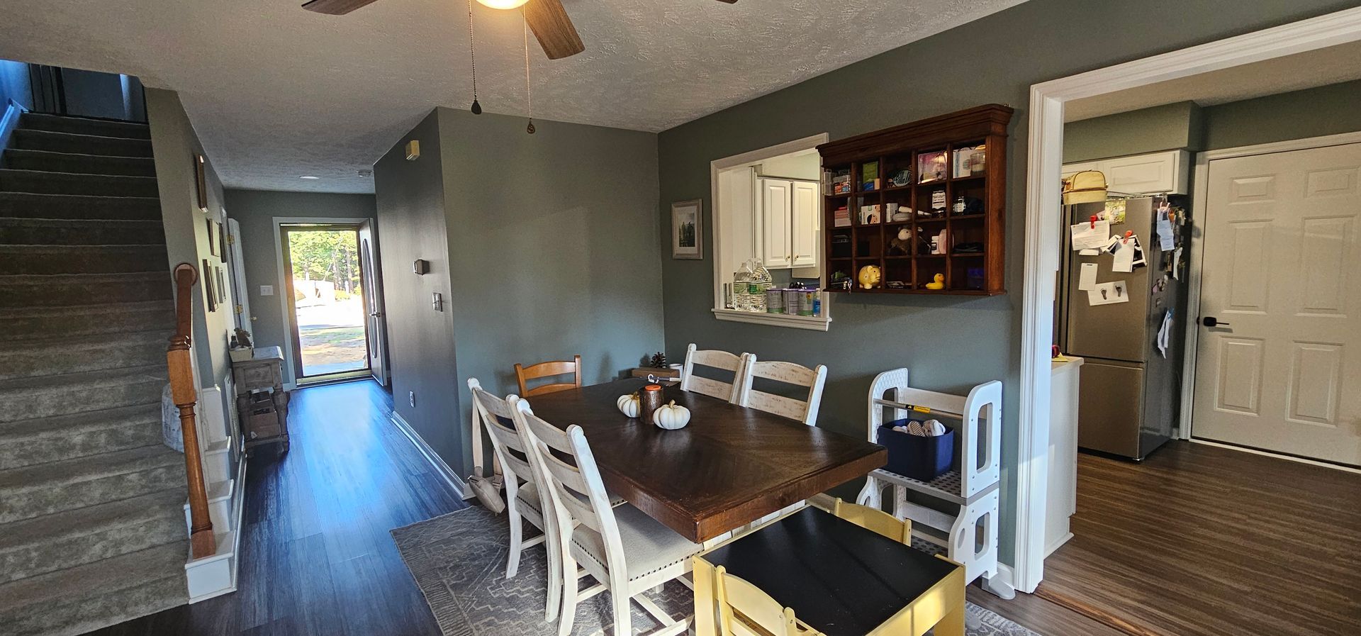 Dining room with wooden table, white chairs, and gray walls leading into a bright hallway.