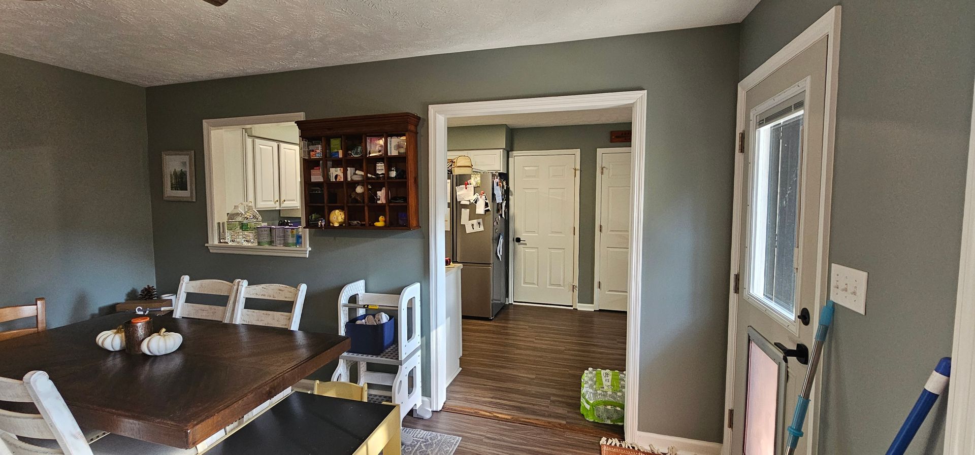 Dining room and kitchen view with wooden table, chairs, gray walls, and white doorways.