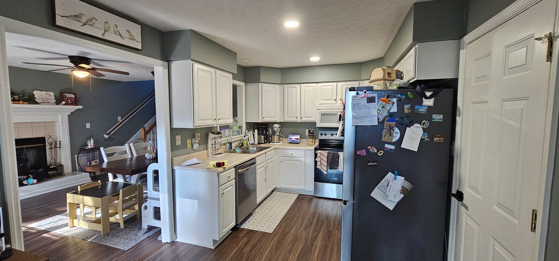 Bright kitchen with white cabinets, black fridge, and hardwood floor, viewed from a doorway.