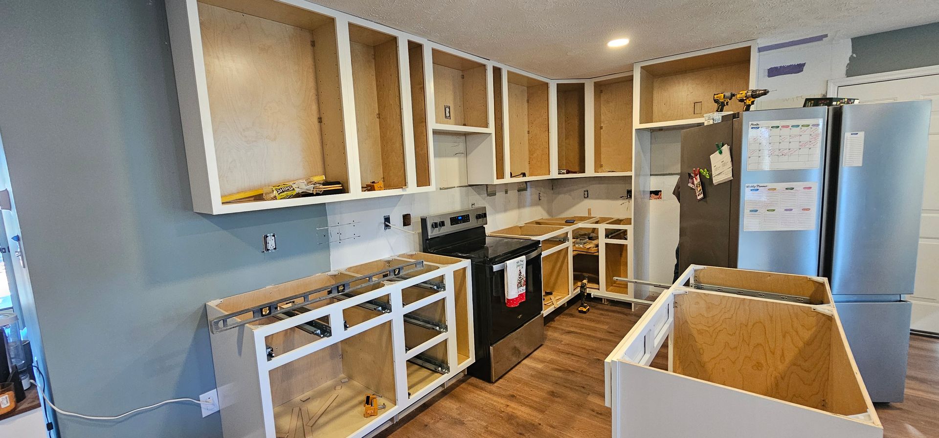 Bright kitchen under renovation with unfinished cabinets, appliances, and cardboard boxes on the floor