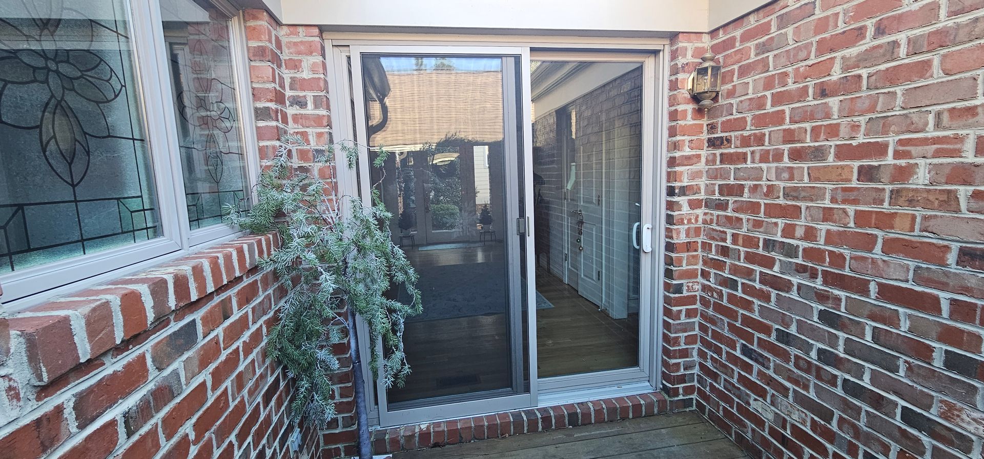 Brick patio with sliding glass door, window, and potted plant beside a screened entrance