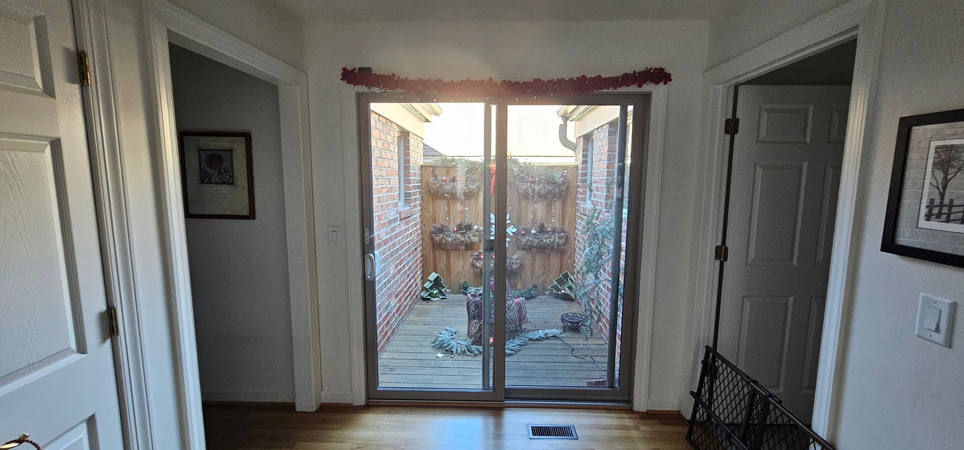 Bright hallway with wooden floors, white doors, and sliding glass doors opening to a backyard patio