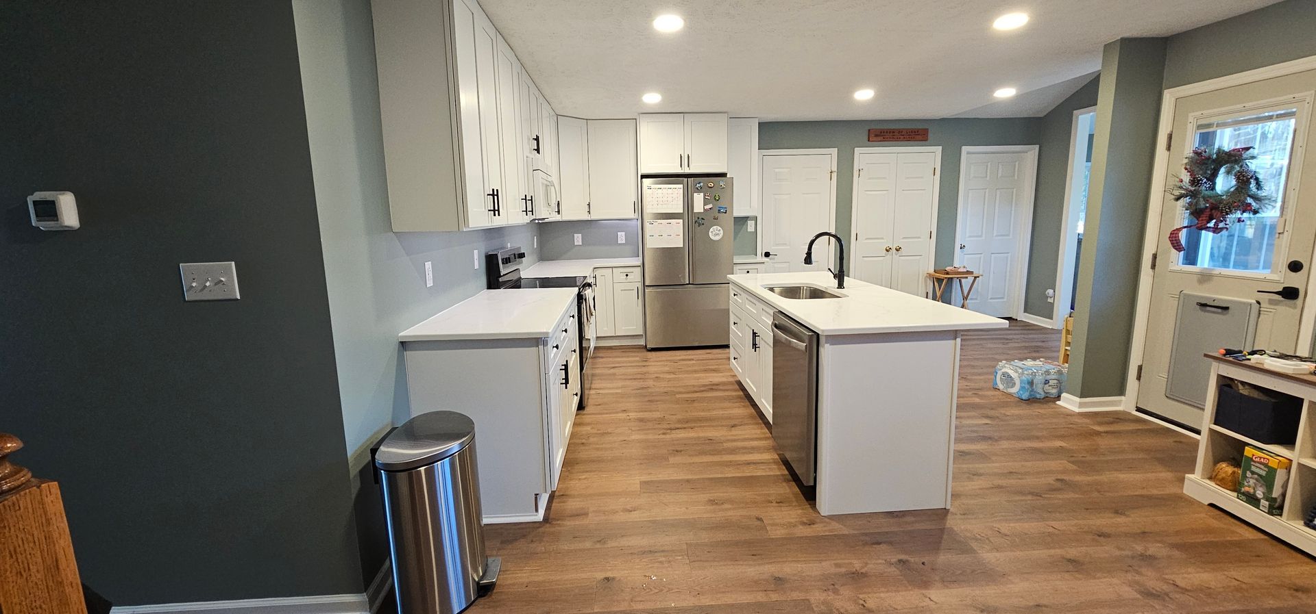 Modern kitchen with white cabinets, island, wood floors, and blue-gray walls in a bright open space