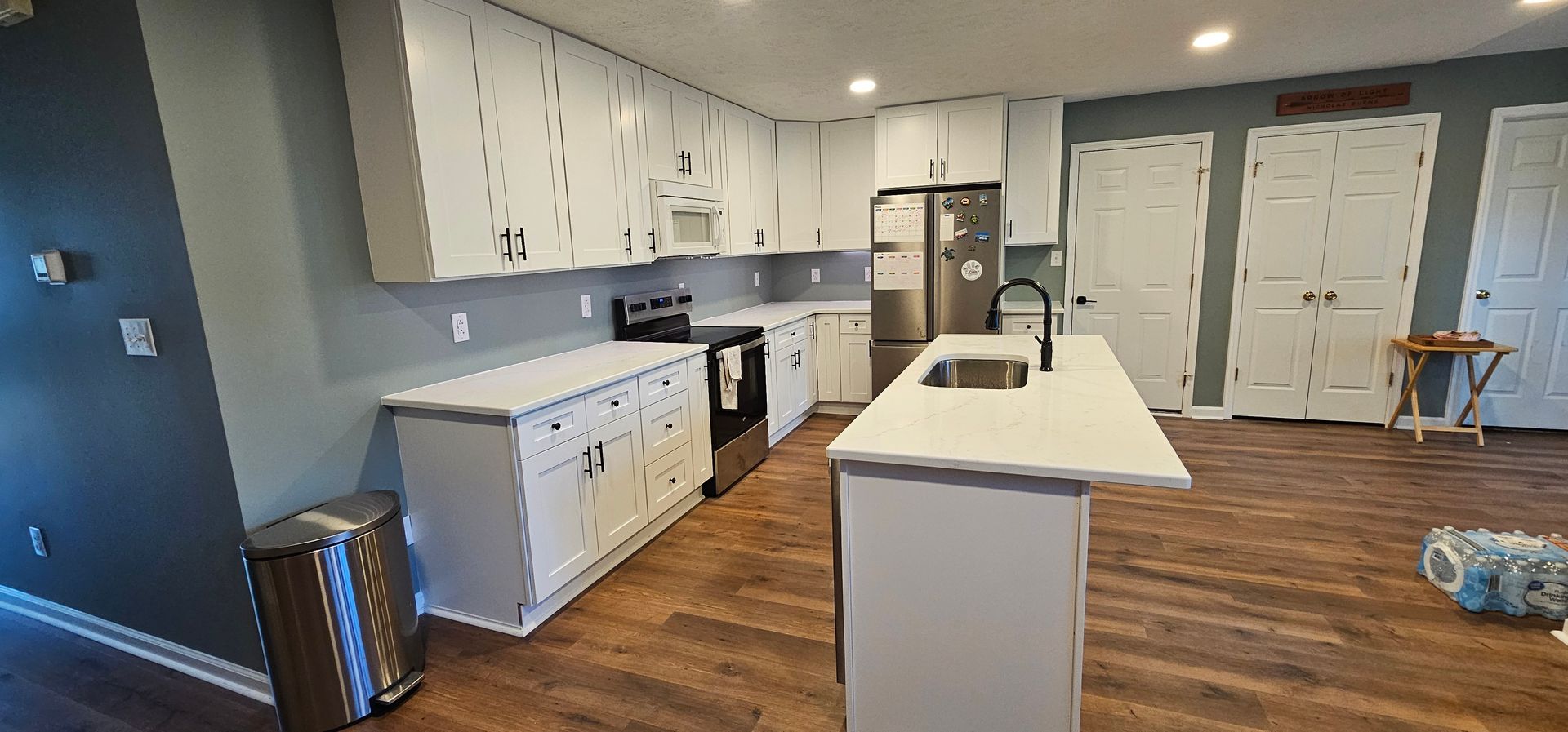 Modern kitchen with white cabinets, island, wood floors, and a dining area in the background