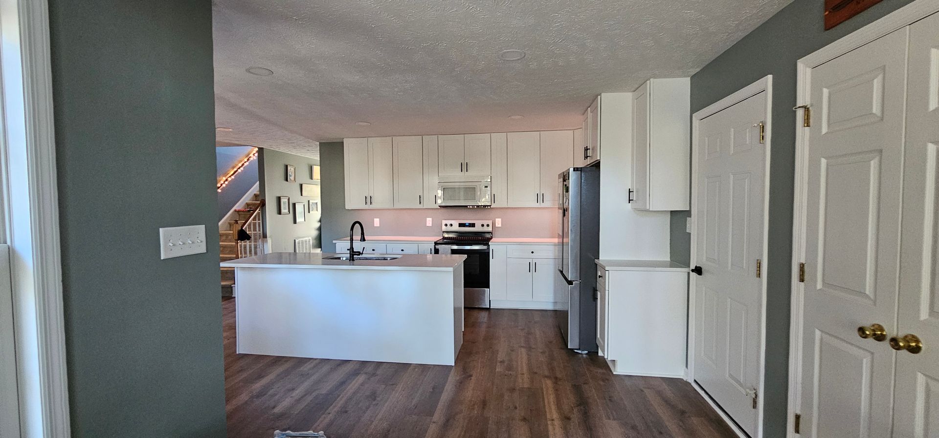 Open-concept kitchen and living area with white cabinets, a gray wall, and wood floors