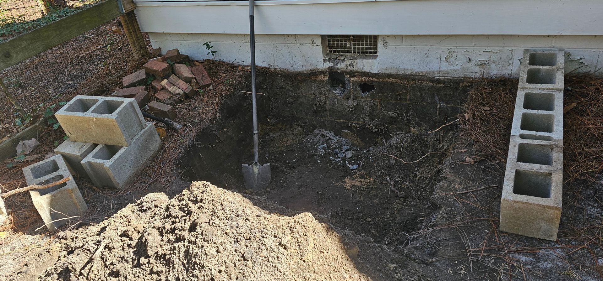 Uneven dirt yard with cinder blocks, a central pole, and a ladder leaning near a concrete structure.