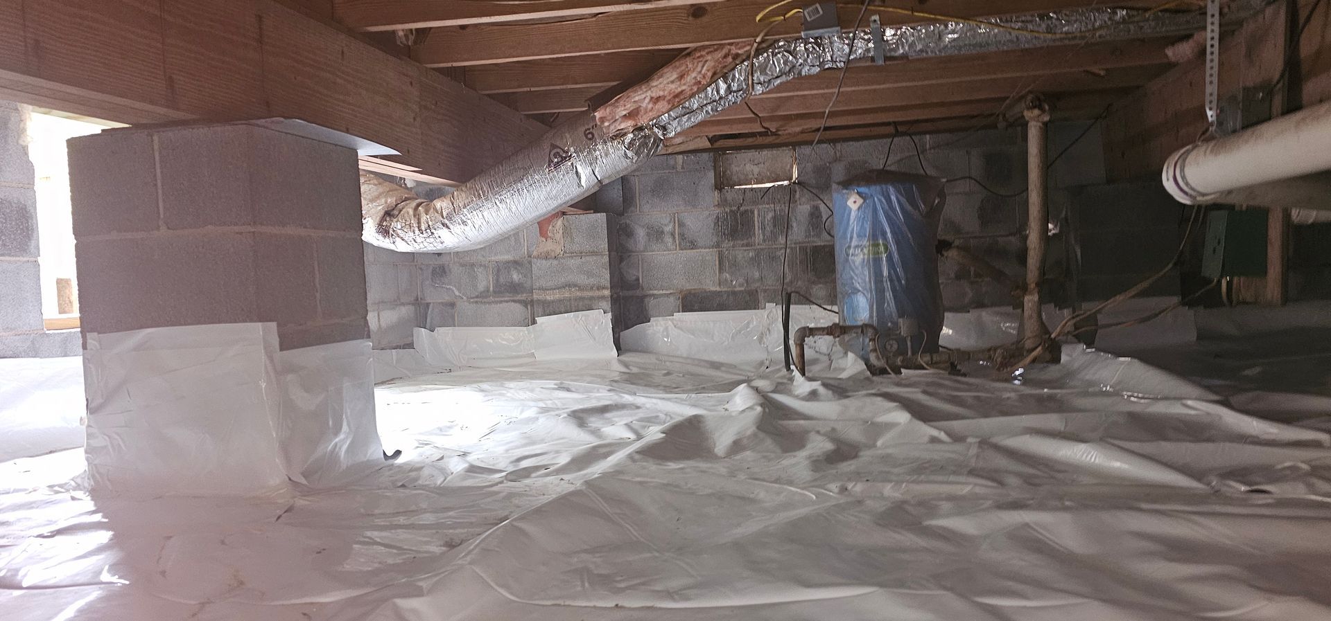 Insulated crawl space with exposed ducts, pipes, and a blue water tank under a wooden floor