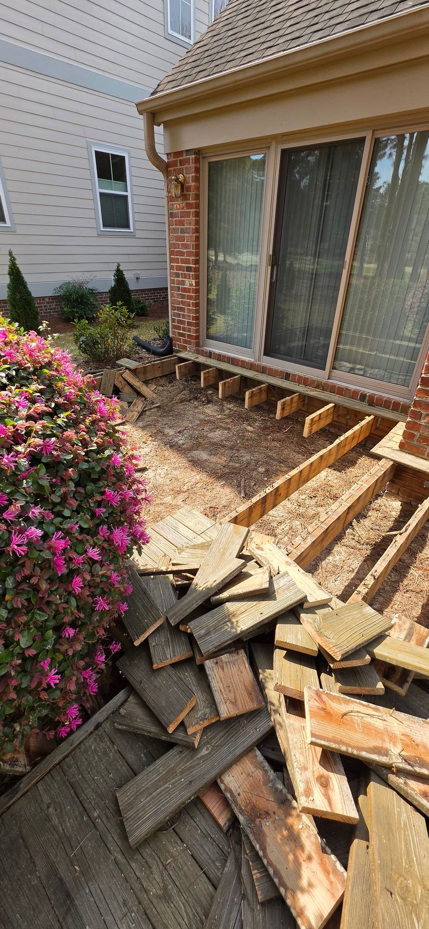 Damaged roof shingles and exposed underlayment beside a house wall and sliding glass door