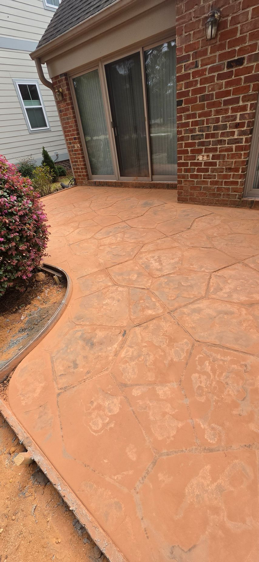 Brick patio beside a house with stamped concrete, sliding glass doors, and a curved flower bed edge