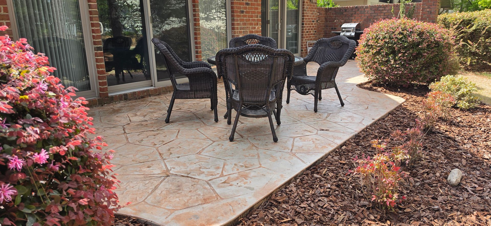 Patio with black metal chairs and table beside a brick house and landscaped garden bed