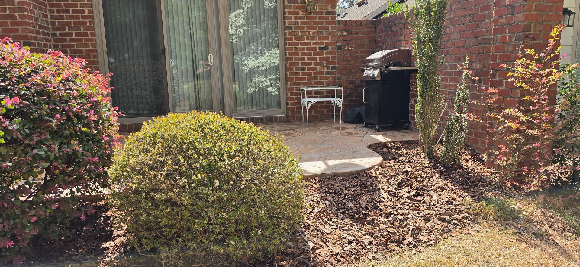 Brick house entry with shrubs and a small patio by the door
