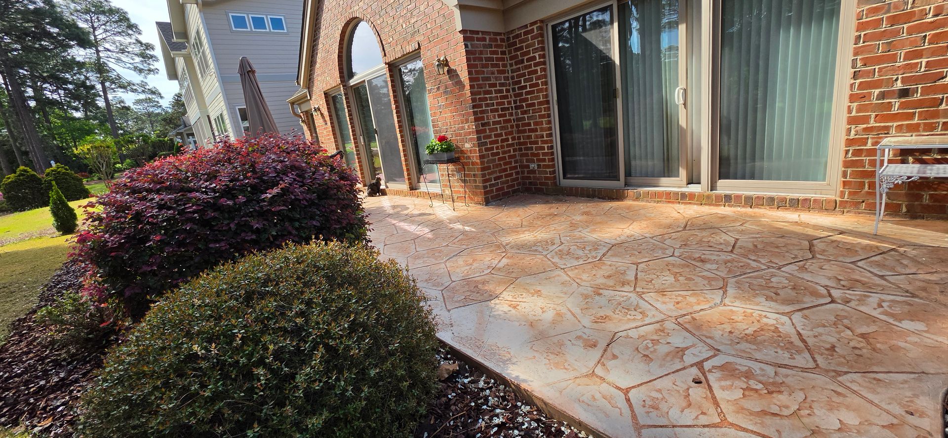 Stone walkway beside landscaped shrubs and brick storefronts with large windows and glass doors