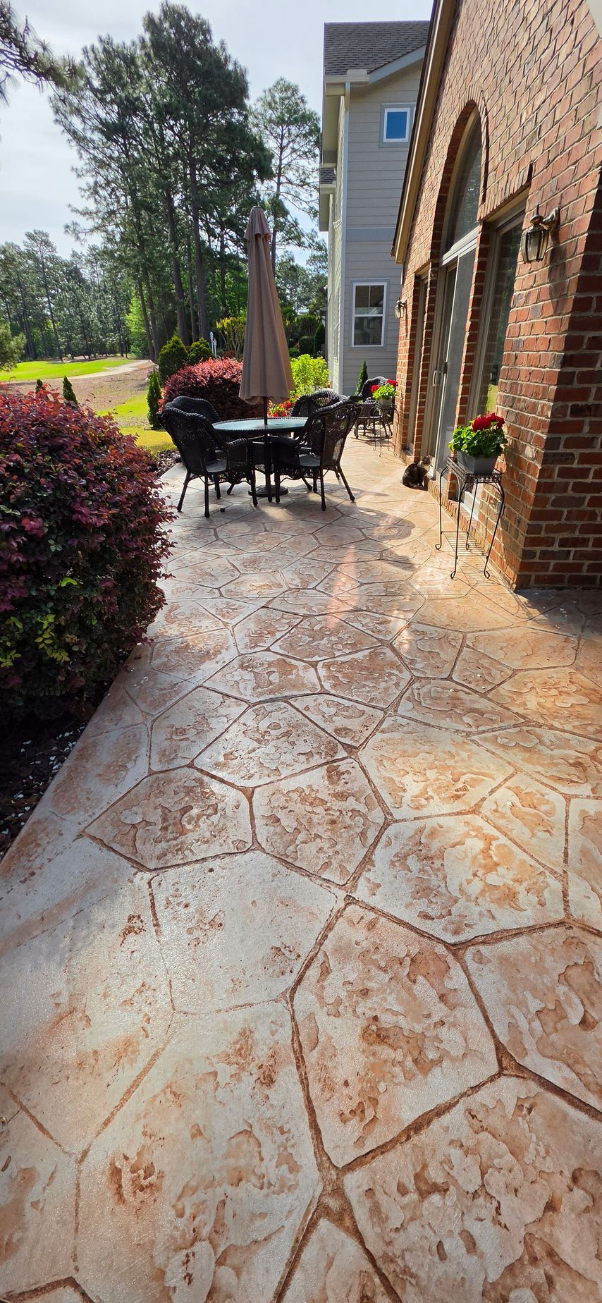 Sunny brick patio beside house with outdoor table, chairs, umbrella, and potted plants