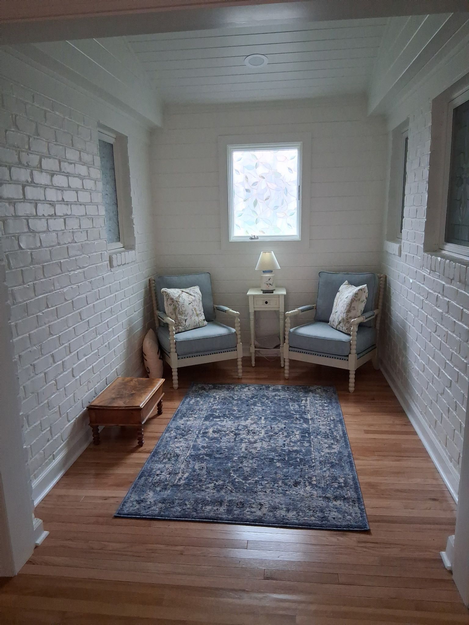 Small cozy sitting room with two chairs, side table, lamp, blue rug, and wooden floor.