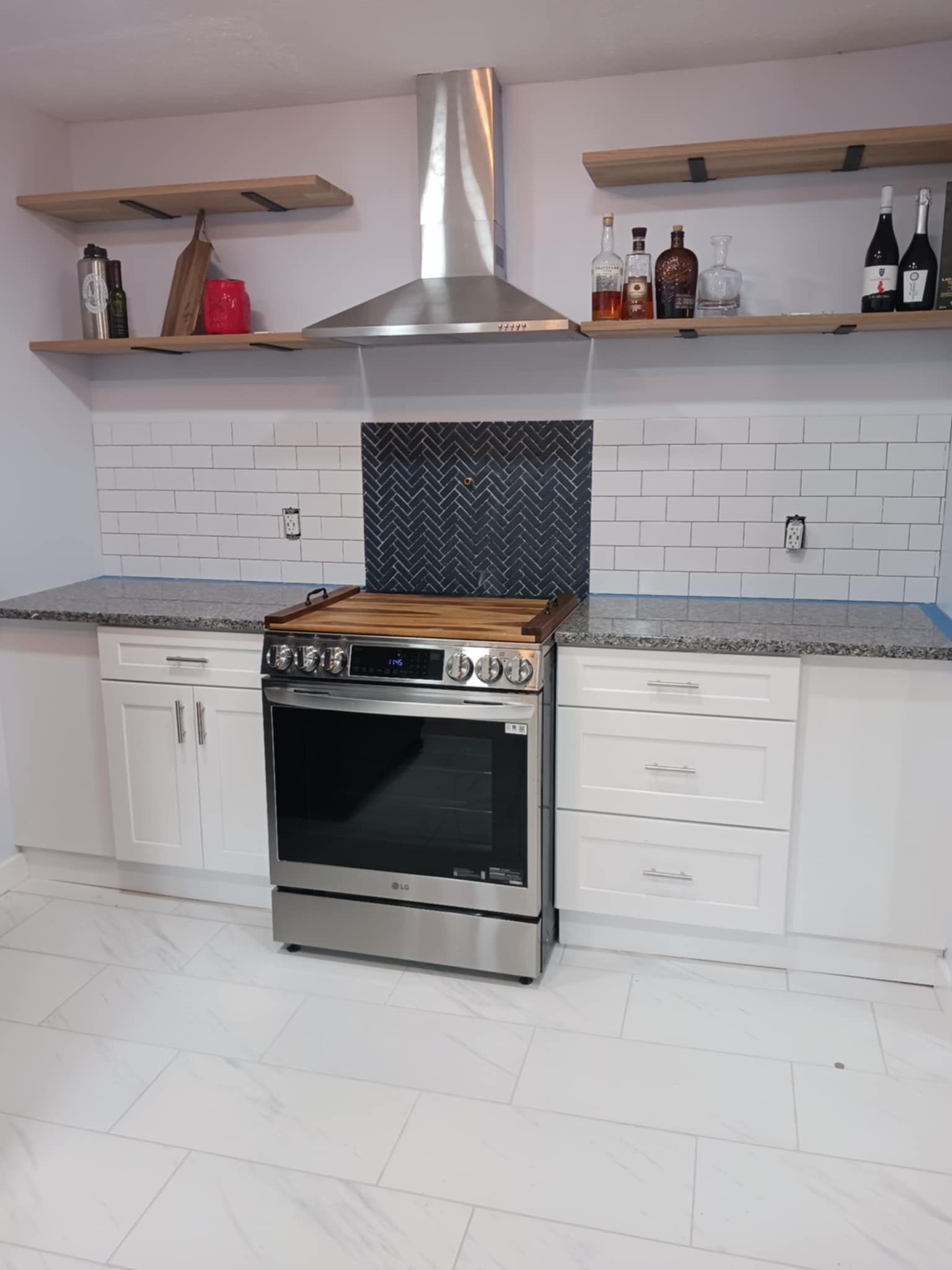 Modern white kitchen with stainless steel stove, hood, subway tile backsplash, and open shelves