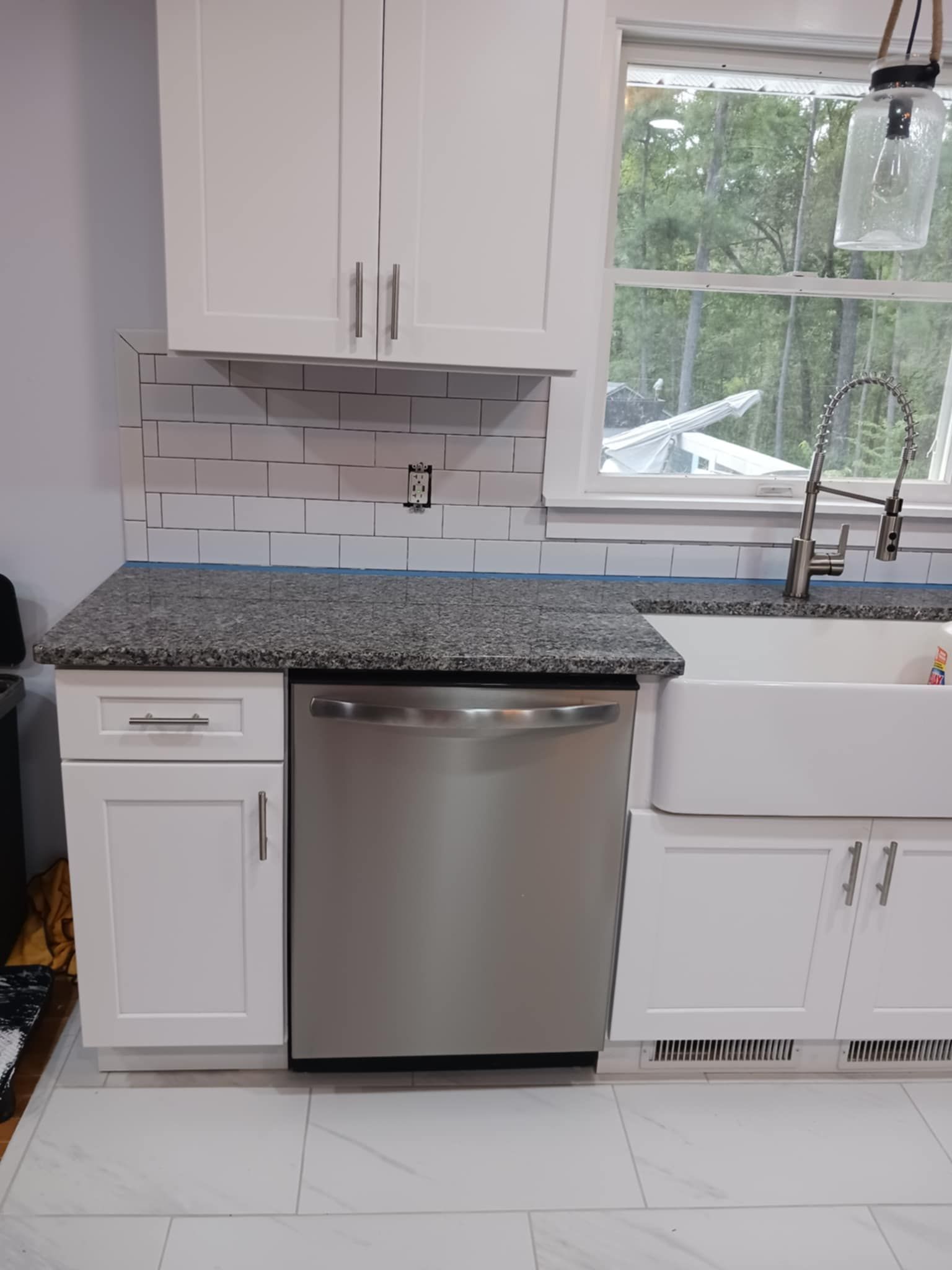 Modern kitchen with white cabinets, stainless dishwasher, marble-look tile floor, and large window over the sink