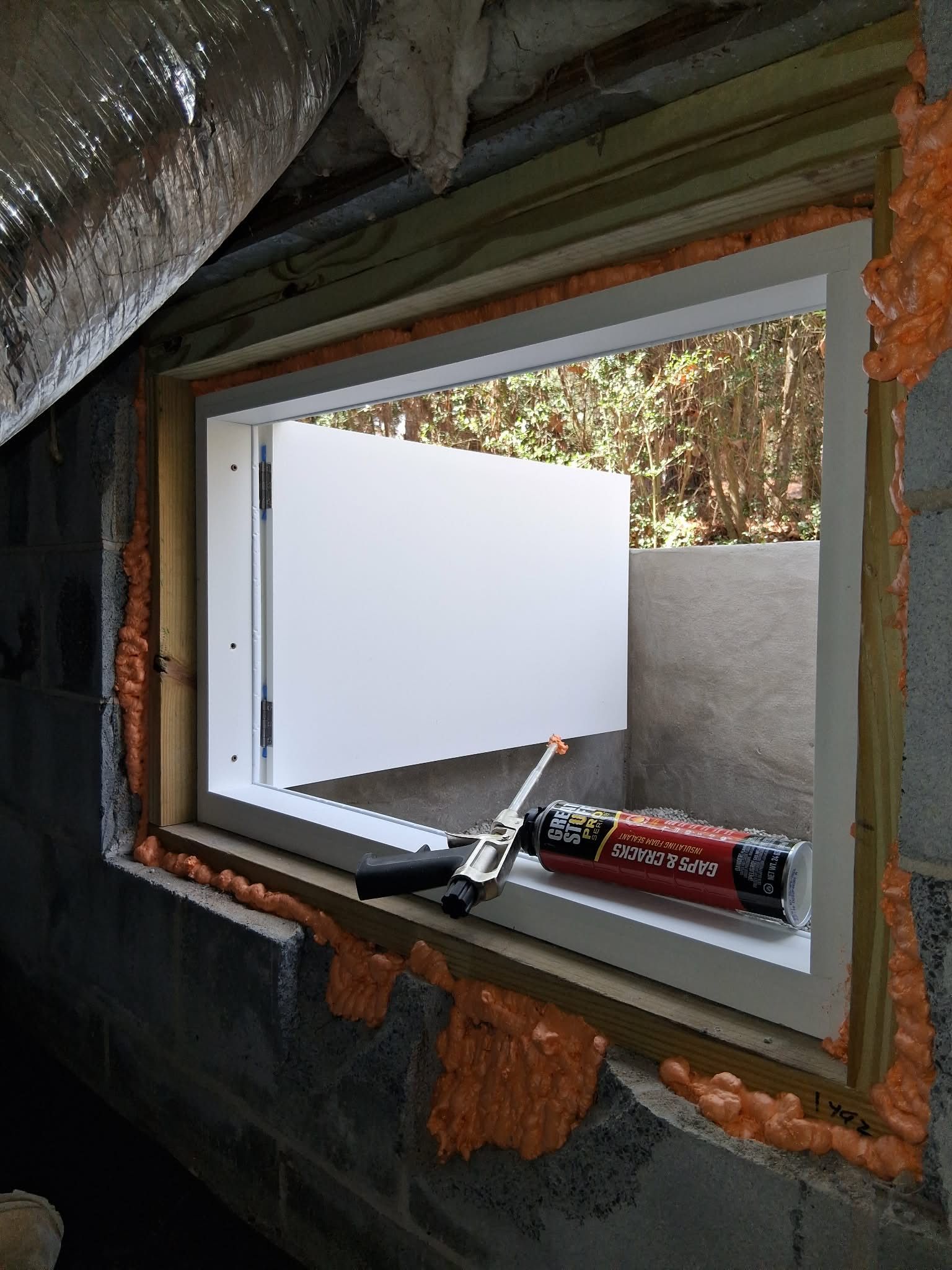 Window opening in a wall under construction, with foam sealant and a caulk gun on the sill.