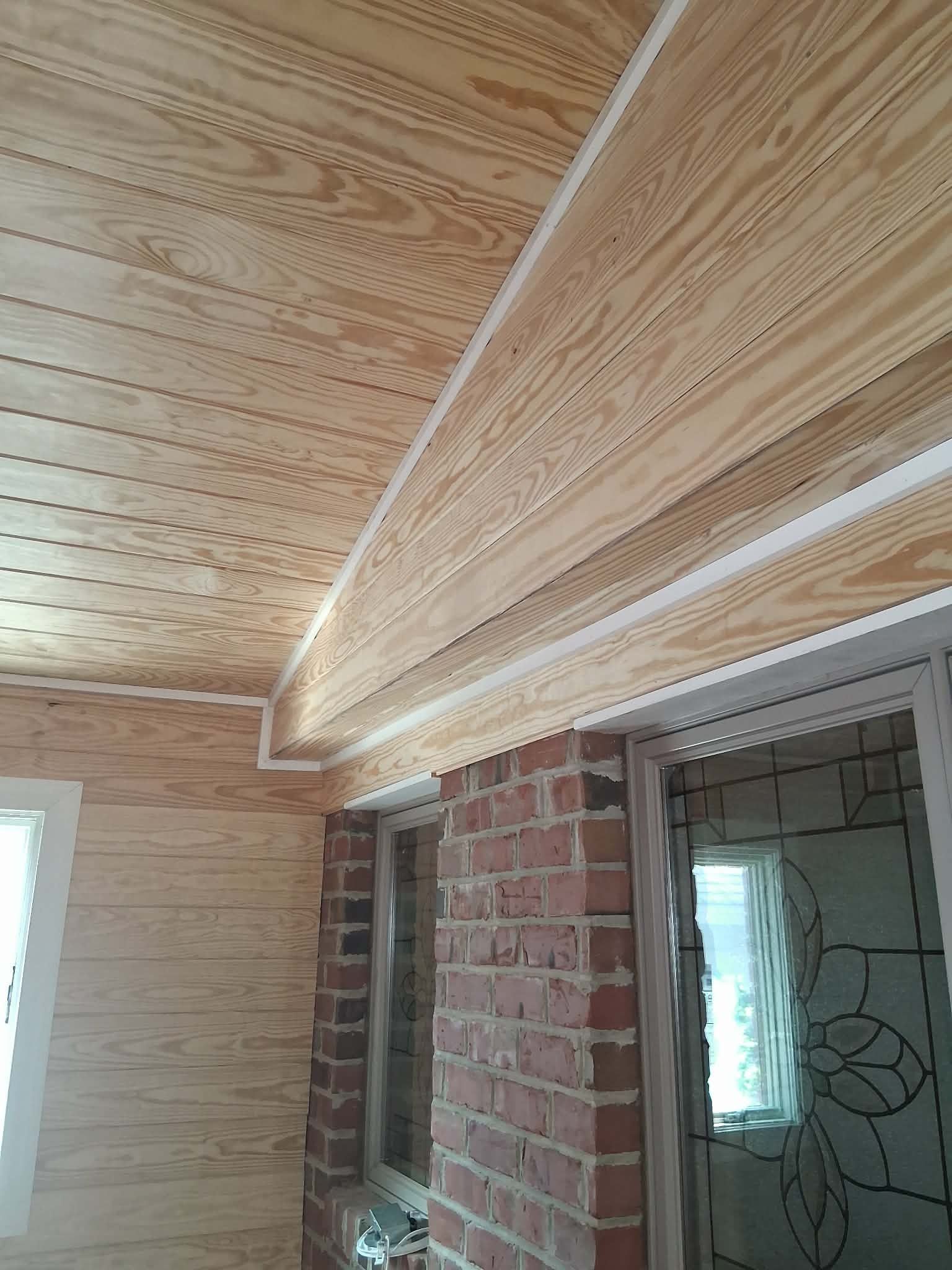 Wood-paneled ceiling and walls in a partially finished room with exposed brick and a doorway.