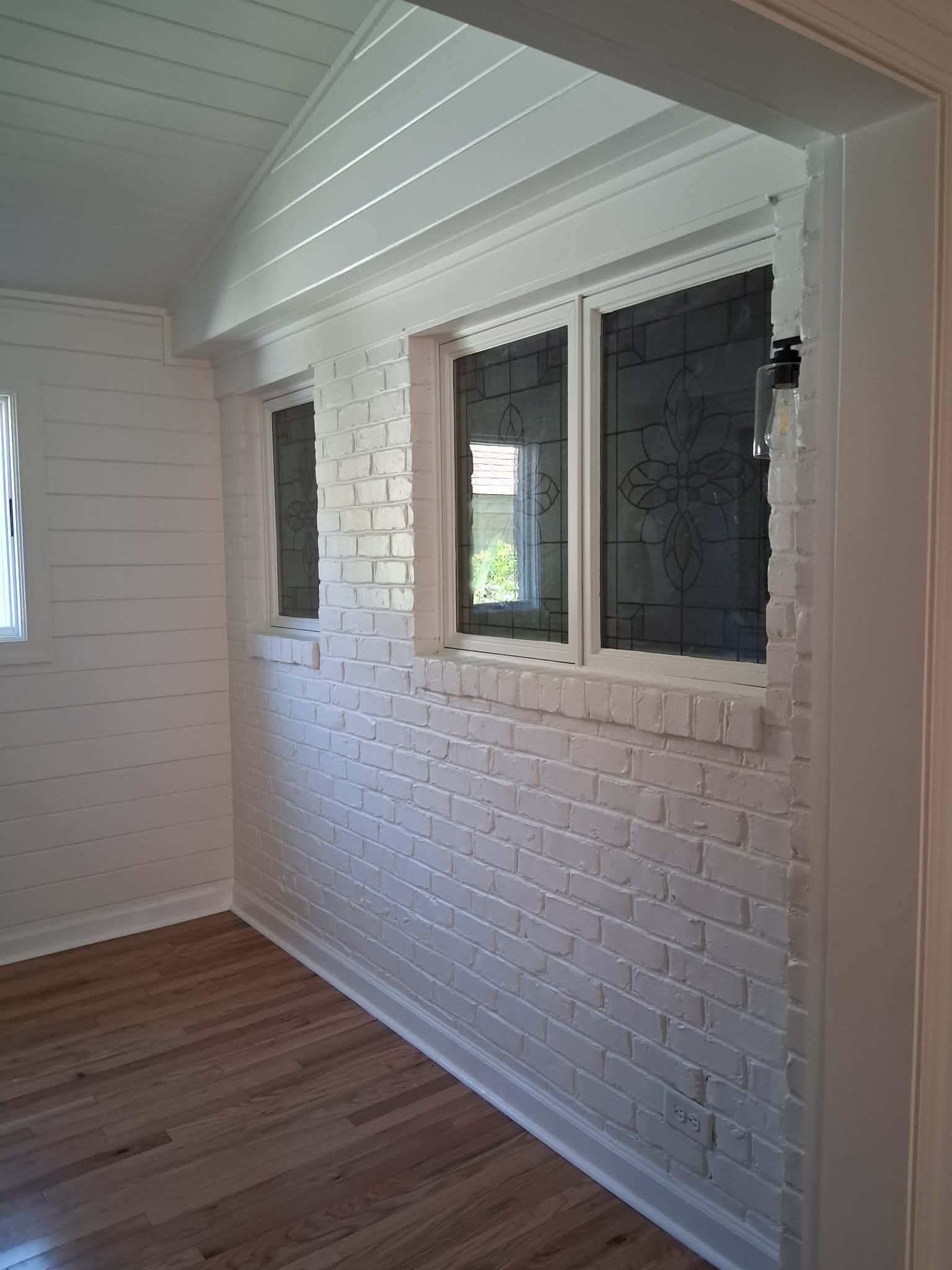 White brick wall with a small window in a bright room, wood floor, and slanted white ceiling panels