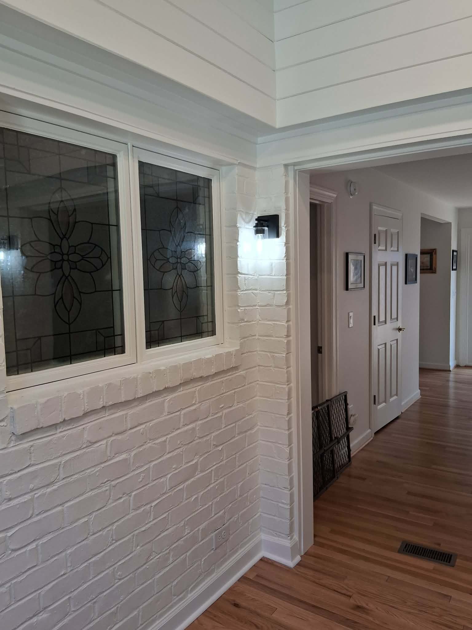 White brick porch corner with windows, entry light, and wood floor leading to a hallway door