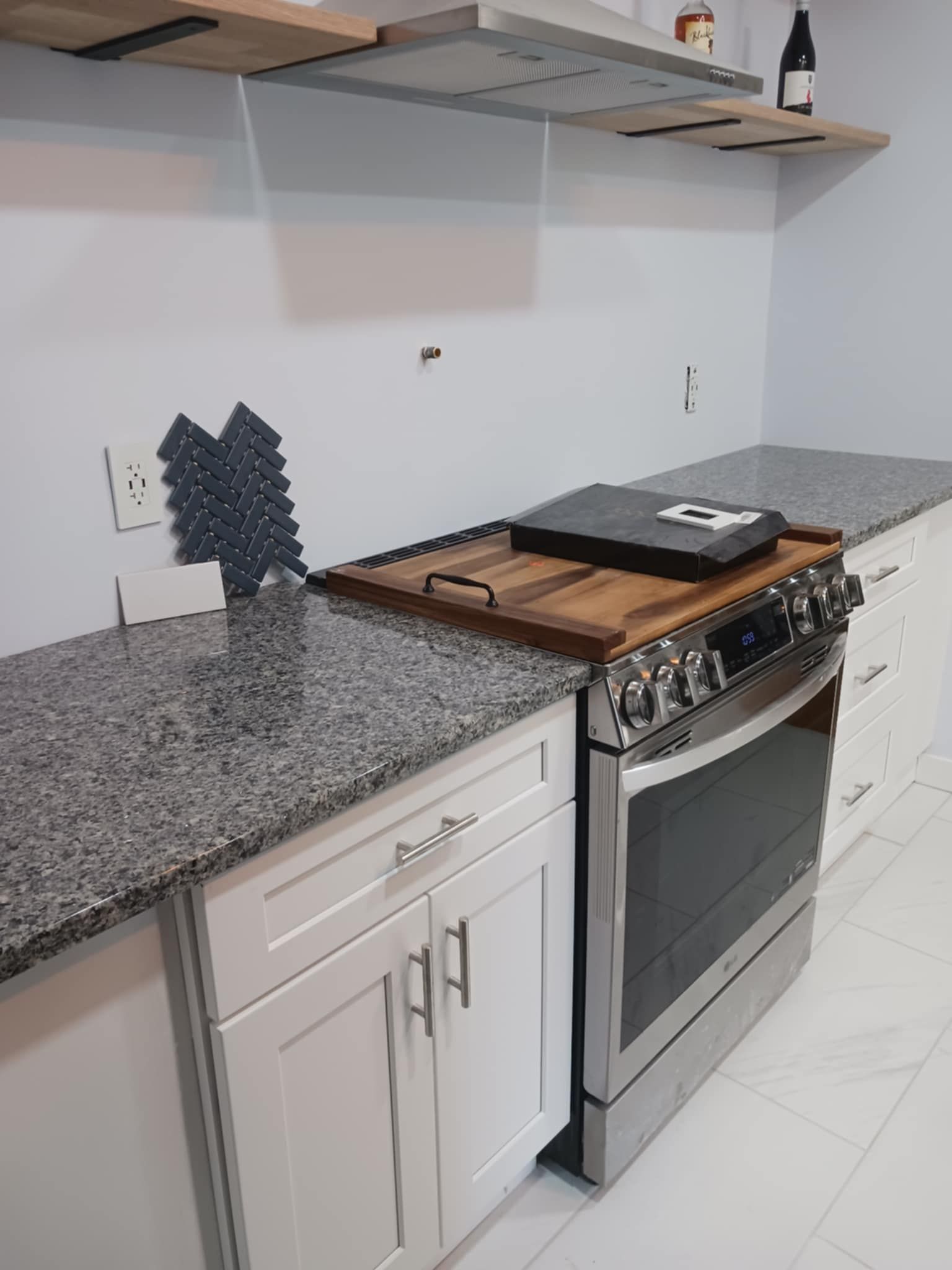 Modern kitchen with granite countertop, stainless steel stove, white cabinets, and floating shelves