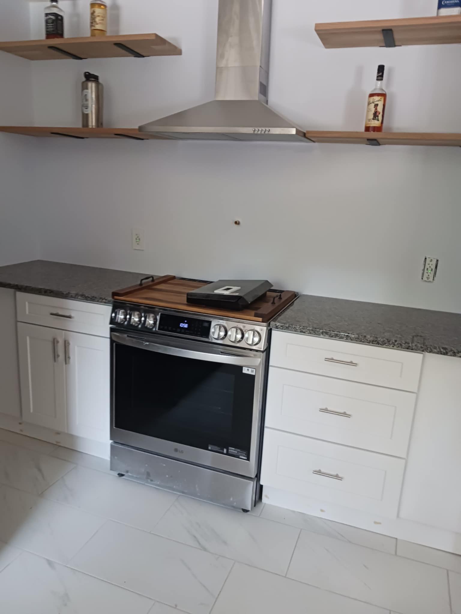 Modern kitchen with white cabinets, gray countertops, stainless steel stove, and floating shelves