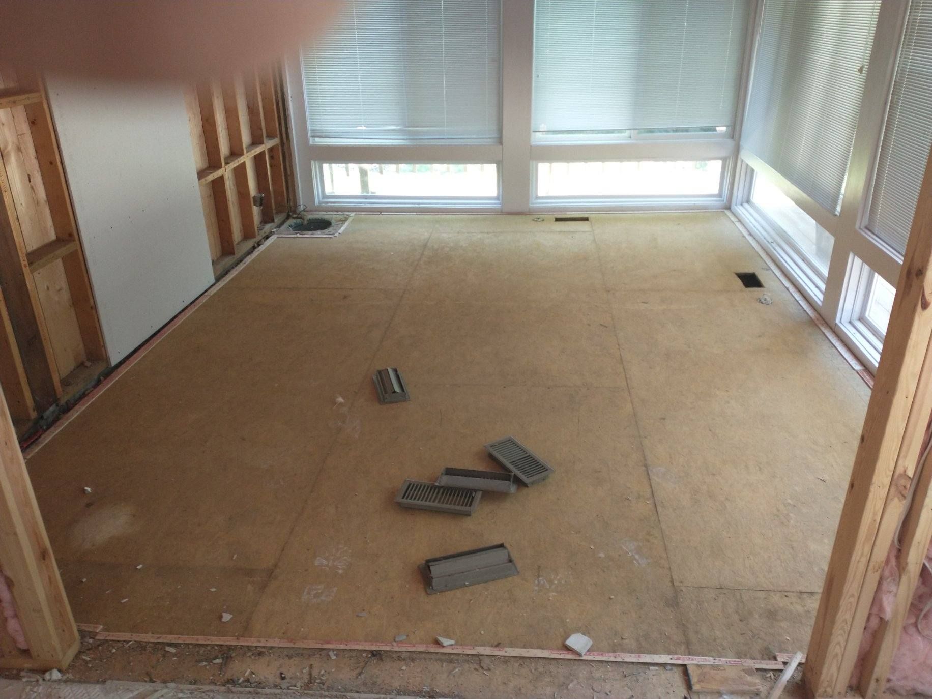 Partially renovated room with bare subfloor and scattered floor boards near windows.