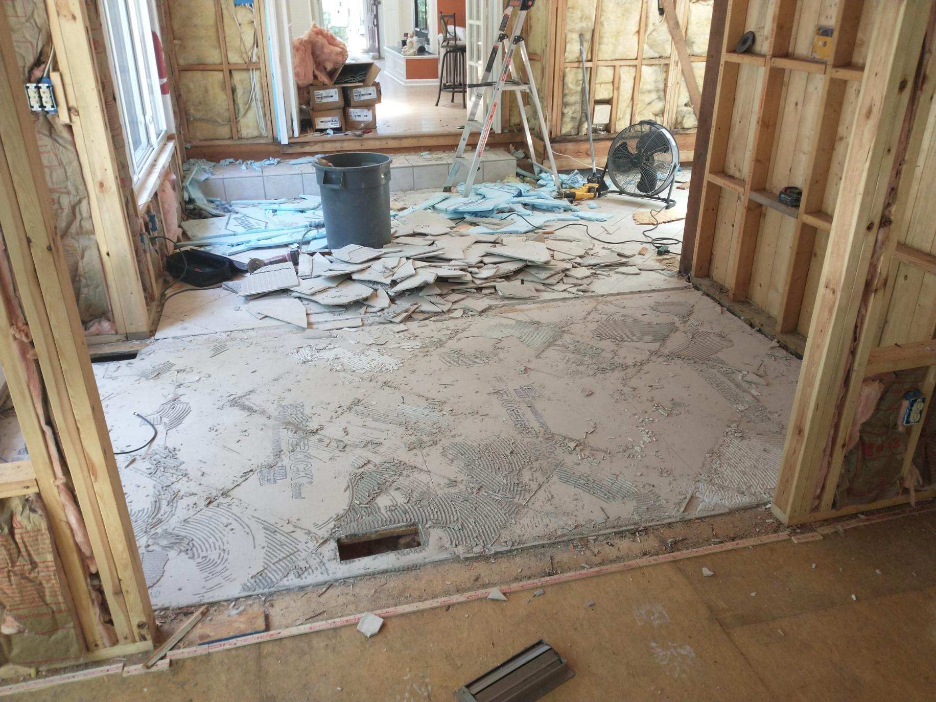 Renovated room with exposed studs, torn flooring, and construction debris scattered across the floor