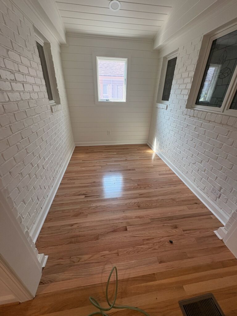 Narrow white hallway with hardwood floor, textured walls, and a single window at the end.