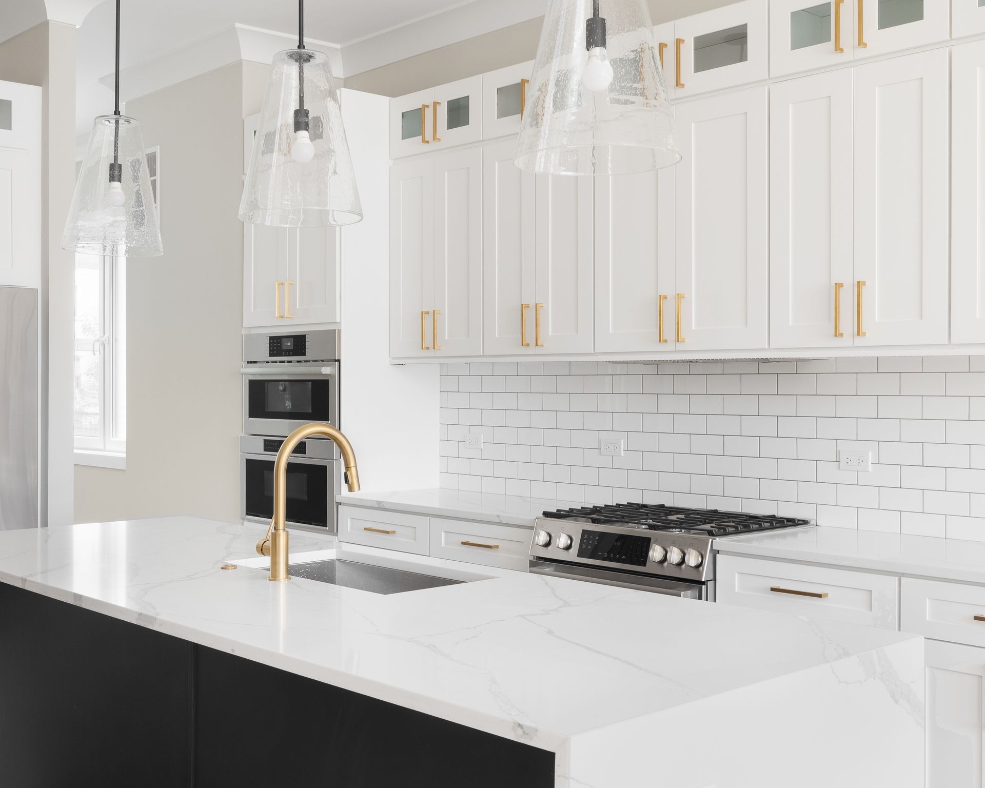 Bright white modern kitchen with gold accents, marble island, and stainless steel appliances