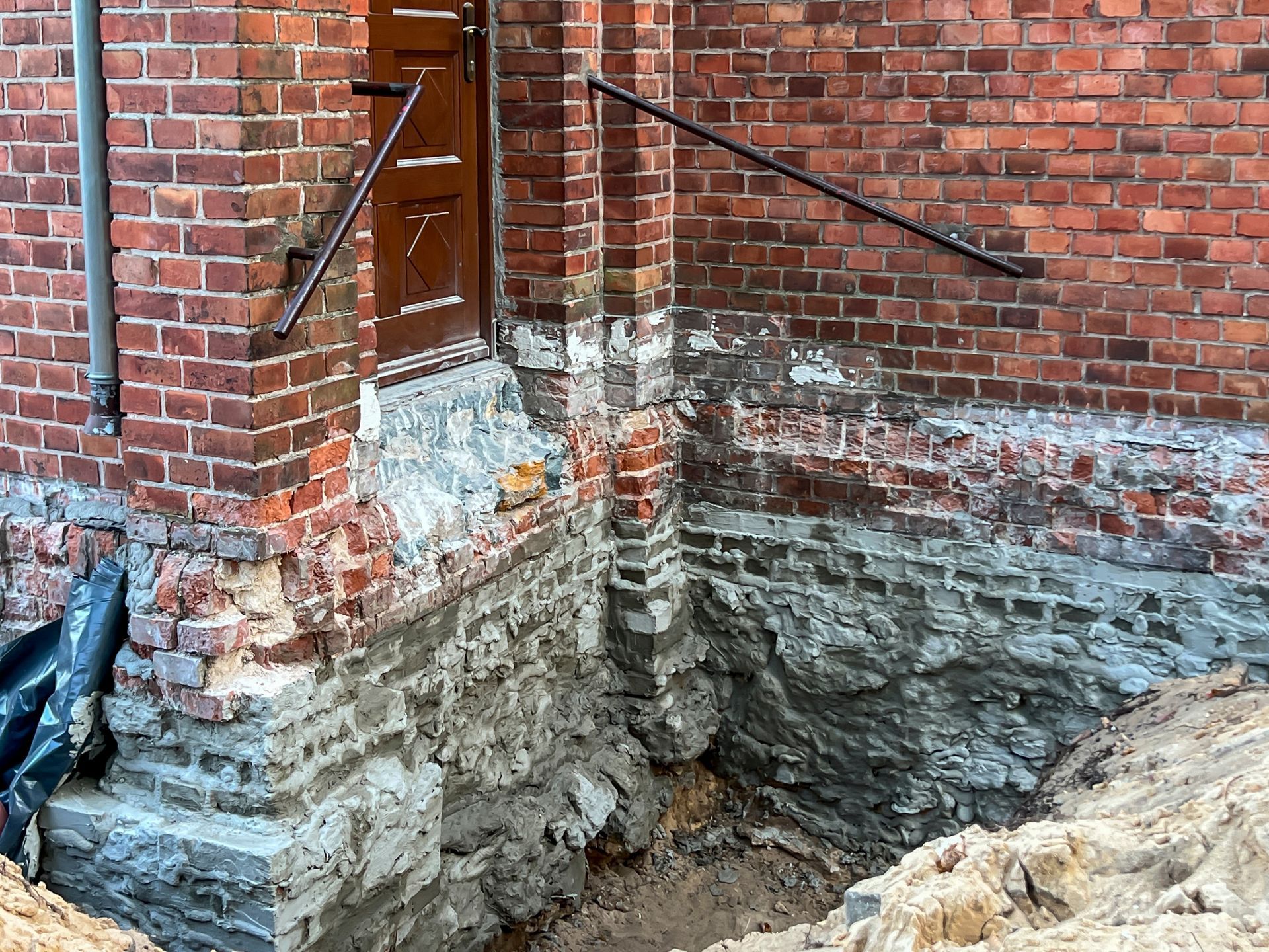 Damaged brick building corner with exposed foundation, rubble, and a partially open door