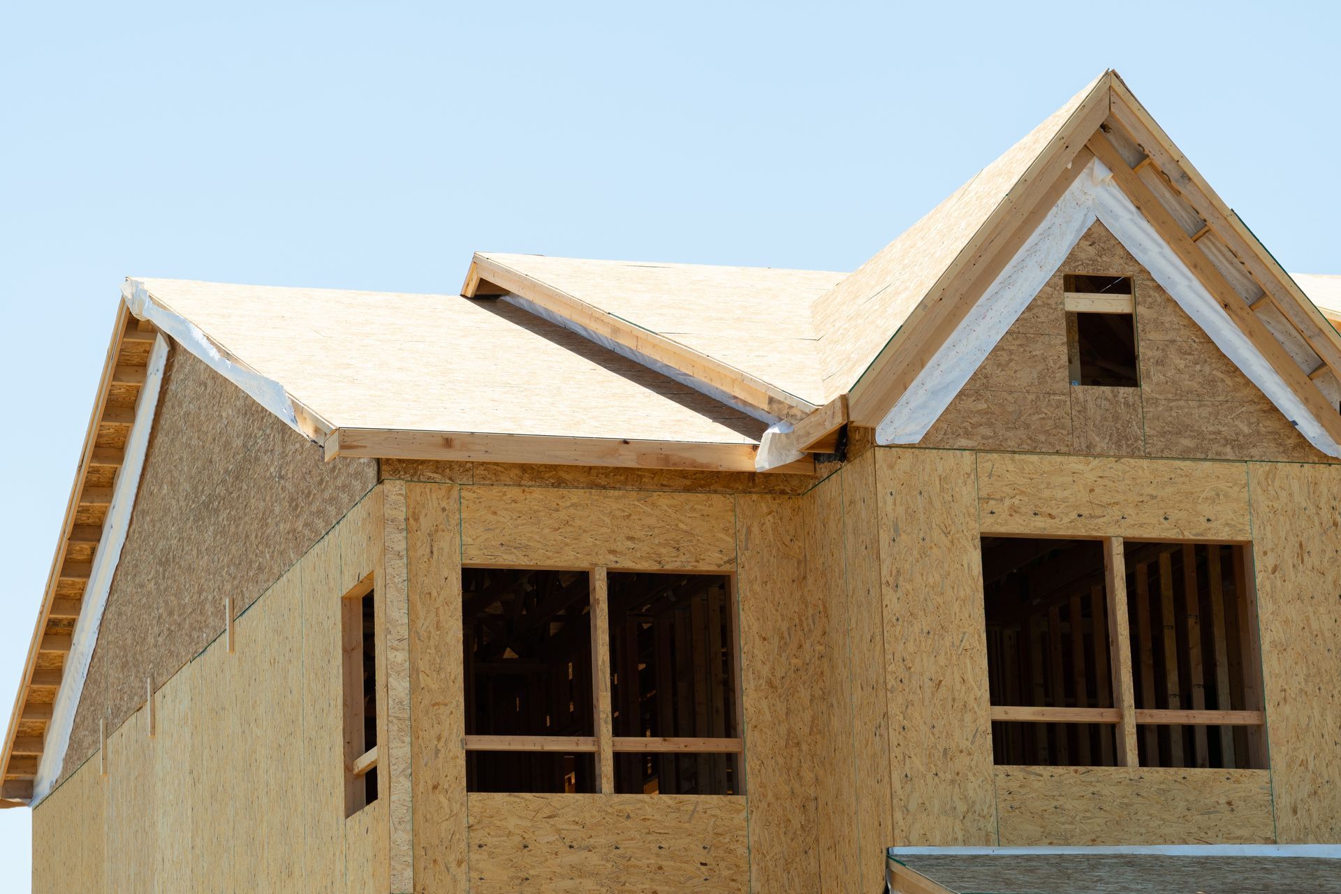 Partially built house with exposed plywood walls and roof framing under a blue sky