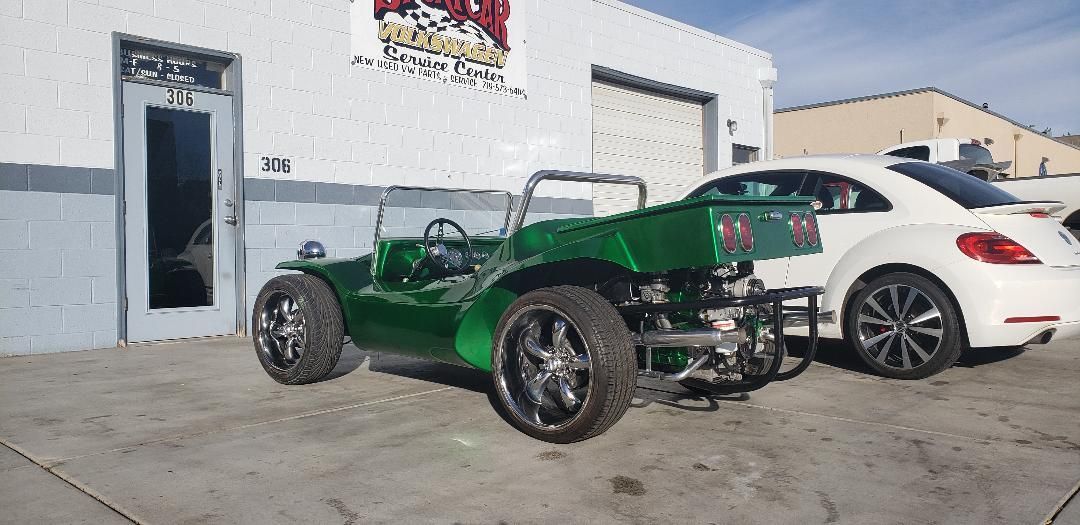 A green buggy and a white car are parked in front of a building.