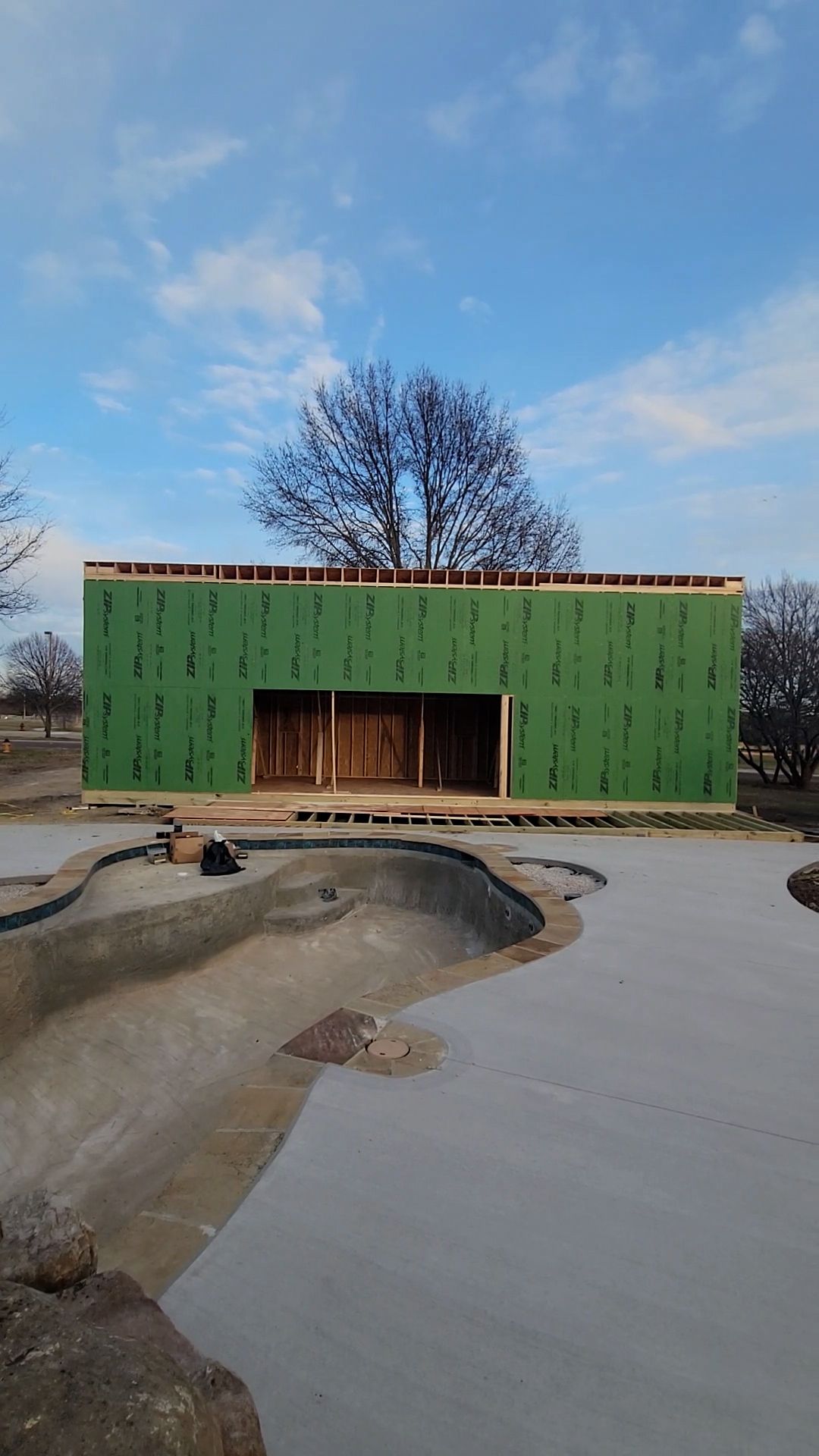 Green-framed unfinished structure beside a curved concrete pathway under a blue sky