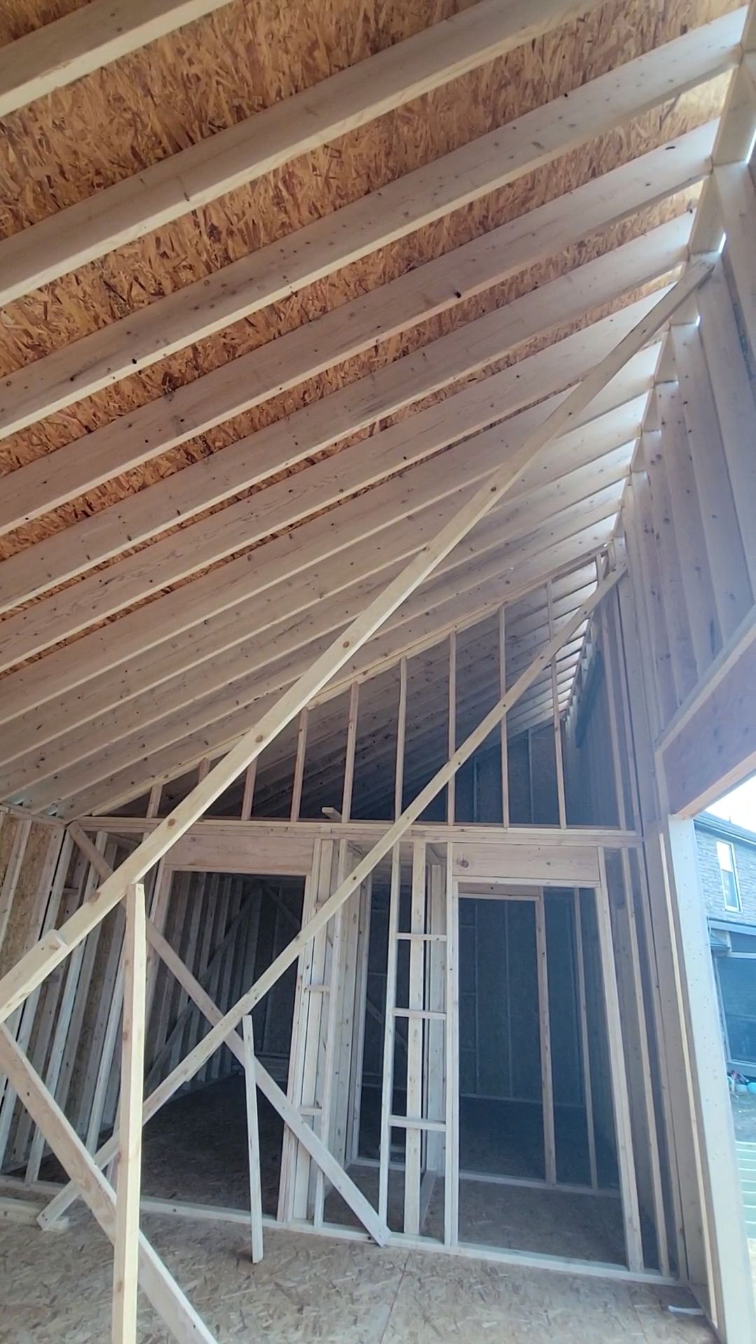 Wood-framed house under construction, with exposed rafters and roof trusses inside.