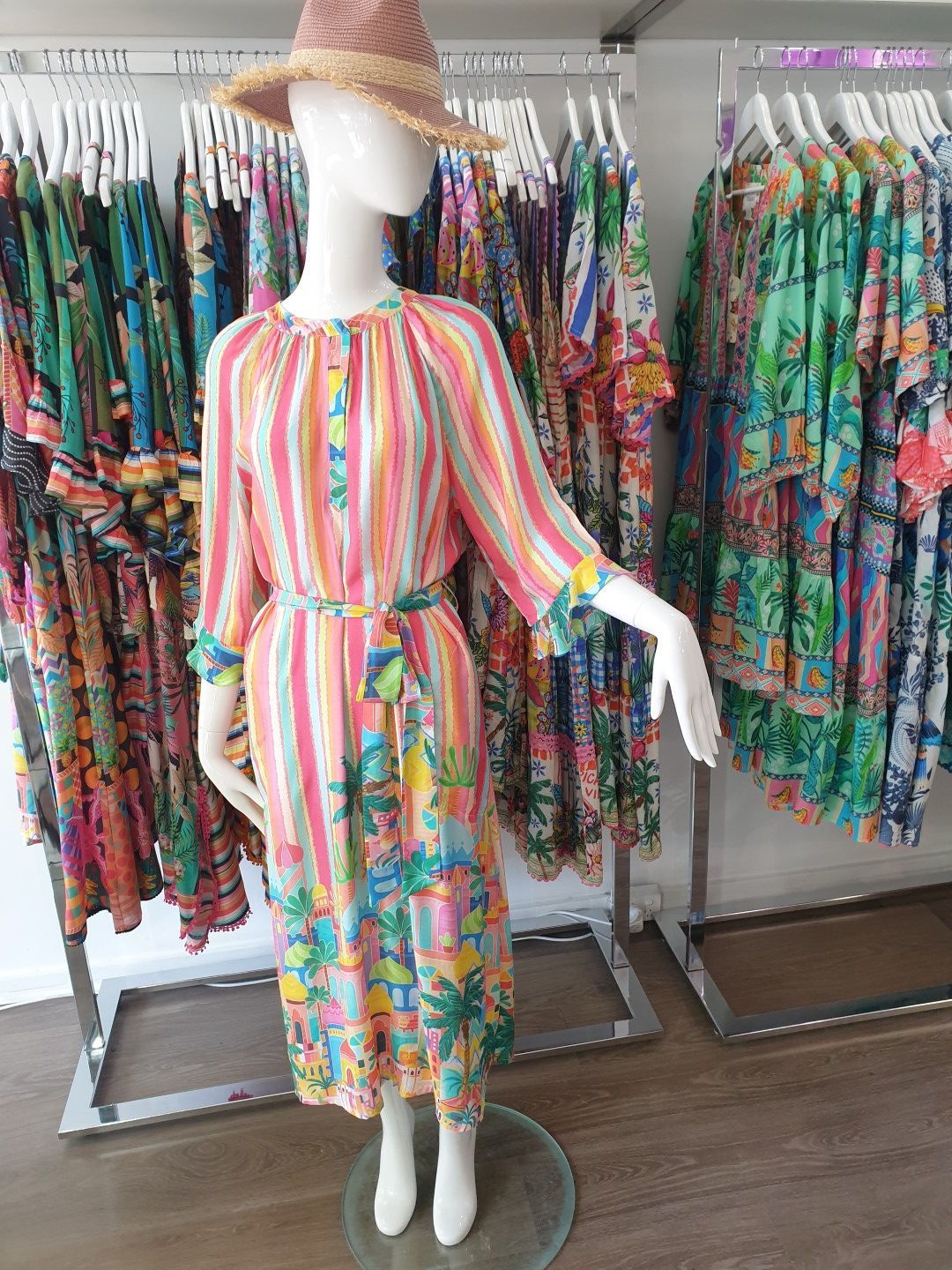 Mannequin in a colorful striped dress and straw hat, surrounded by racks of patterned clothing.