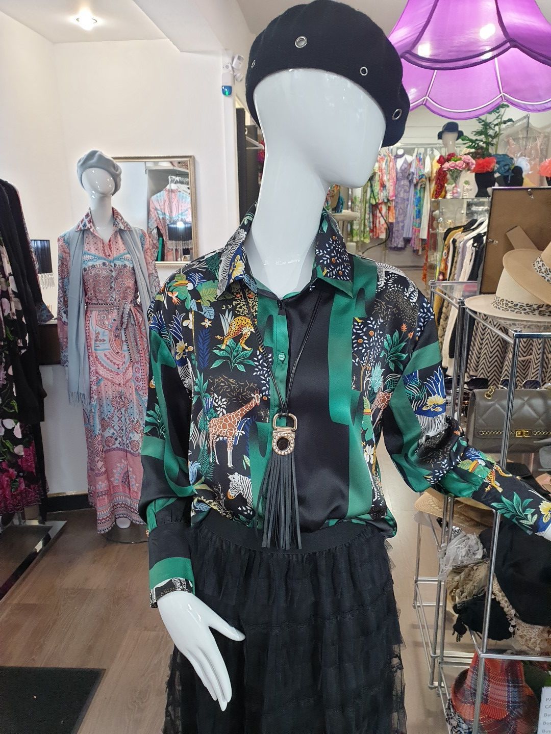 Mannequin in a store window, wearing a floral blouse, black skirt, and beret. Other mannequins and clothing in background.