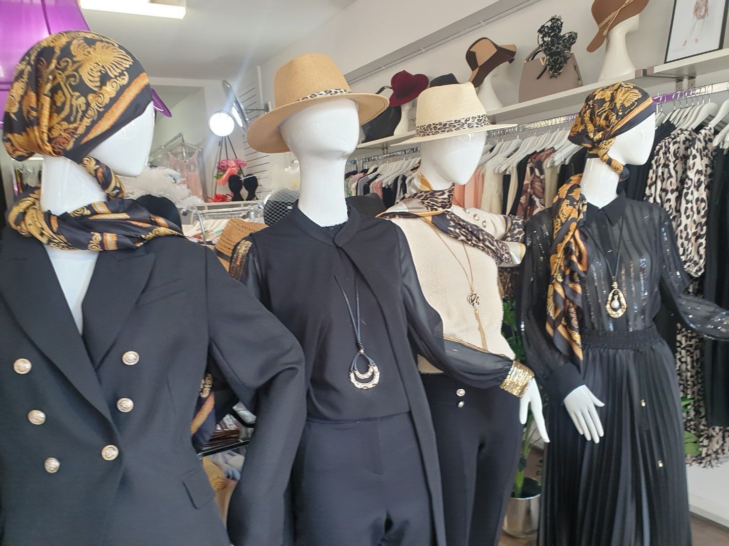 Four mannequins in a clothing store wearing stylish outfits and hats. Gold and black accents with a neutral background.