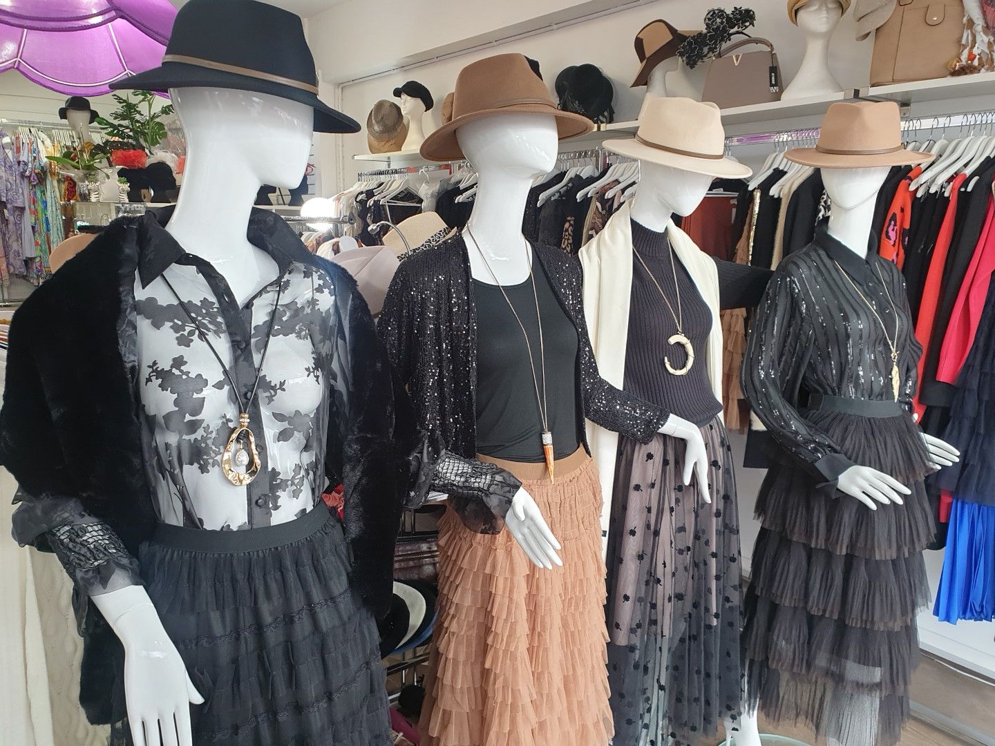 Four mannequins wearing hats and various outfits in a clothing store; neutral colors predominate.