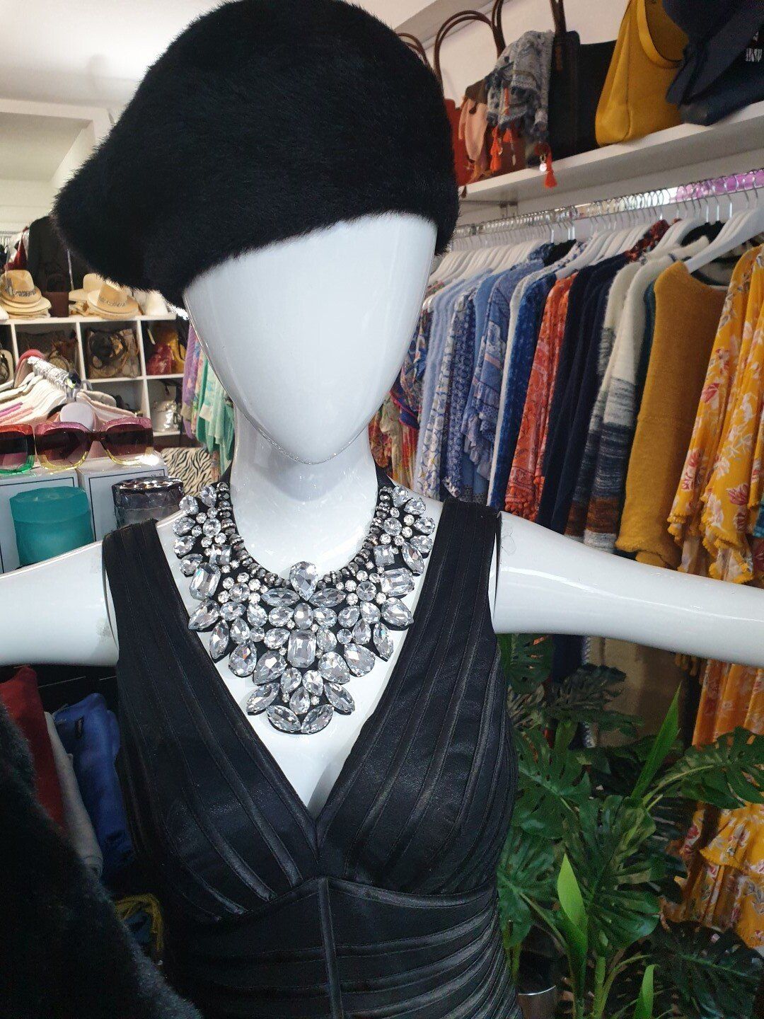 Mannequin in black dress, beret, and jeweled necklace in a clothing store.