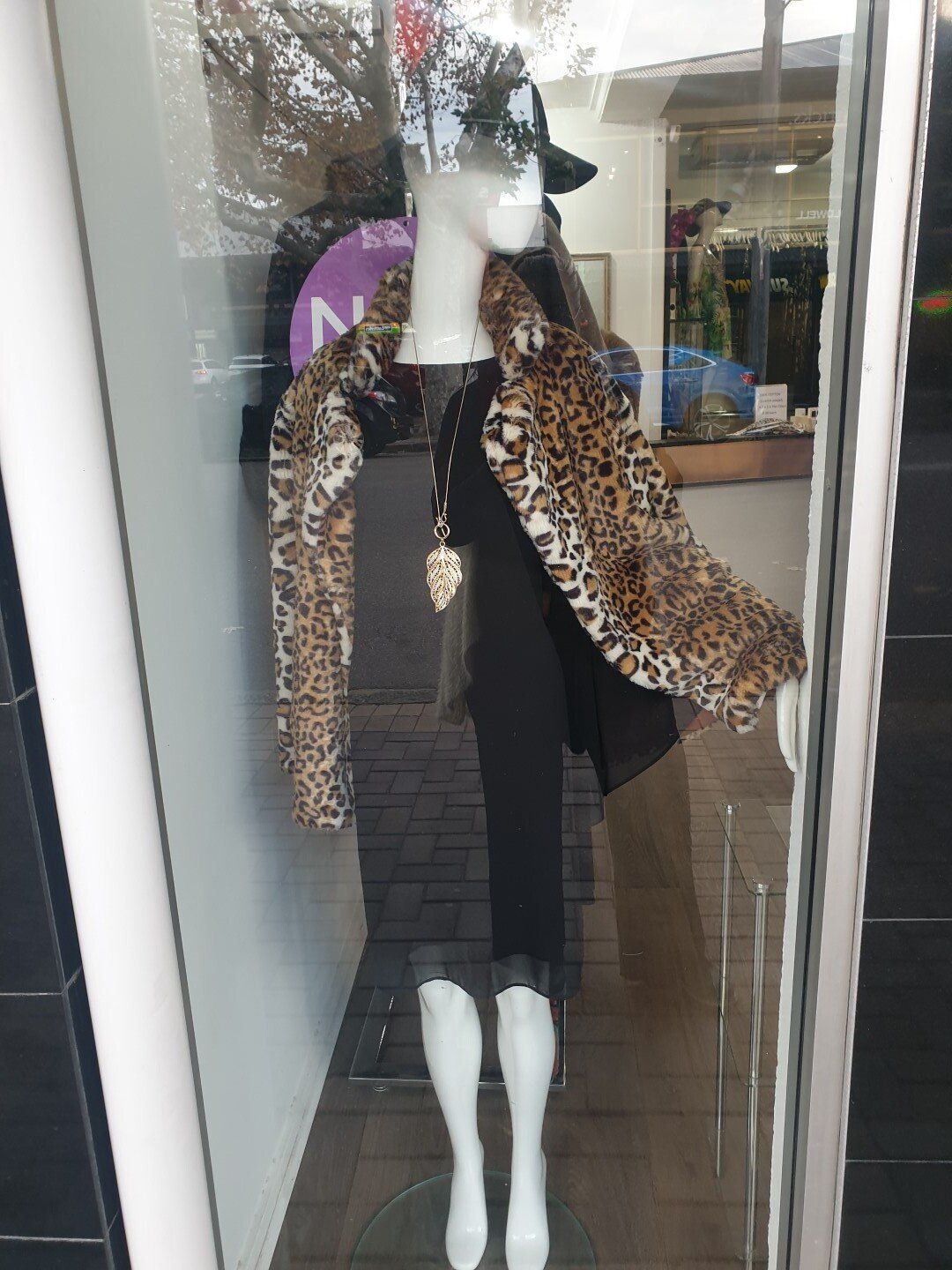 Mannequin in a shop window wearing a black outfit and leopard print scarf.