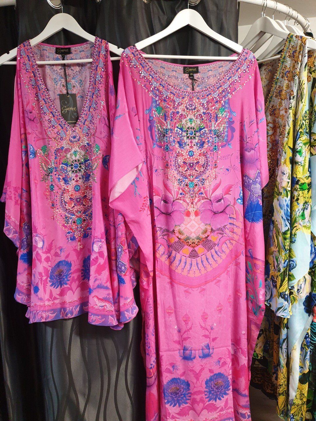 Two vibrant pink kaftans with intricate floral patterns hanging in a clothing store.
