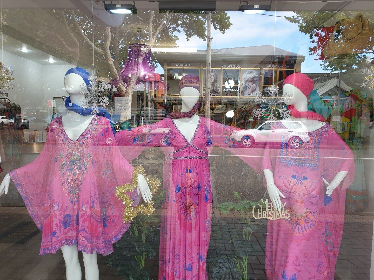 Three mannequins in a store window wearing pink dresses, headscarves, and accessories.