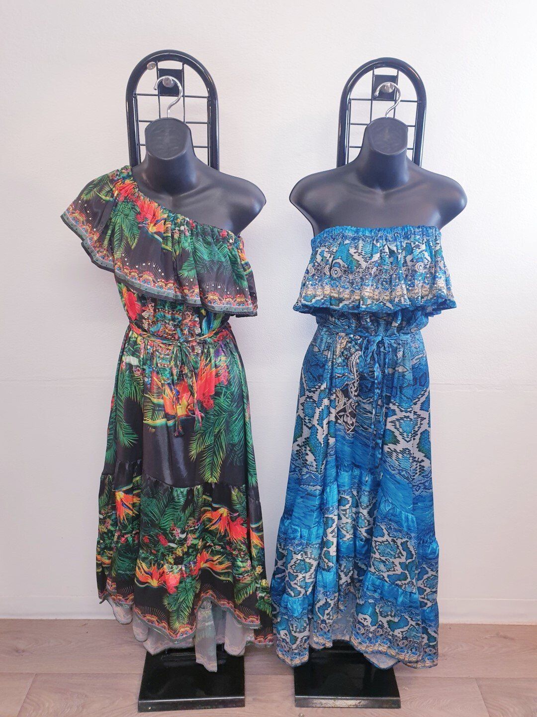 Two dresses on mannequins: one-shoulder tropical print, one strapless blue print.