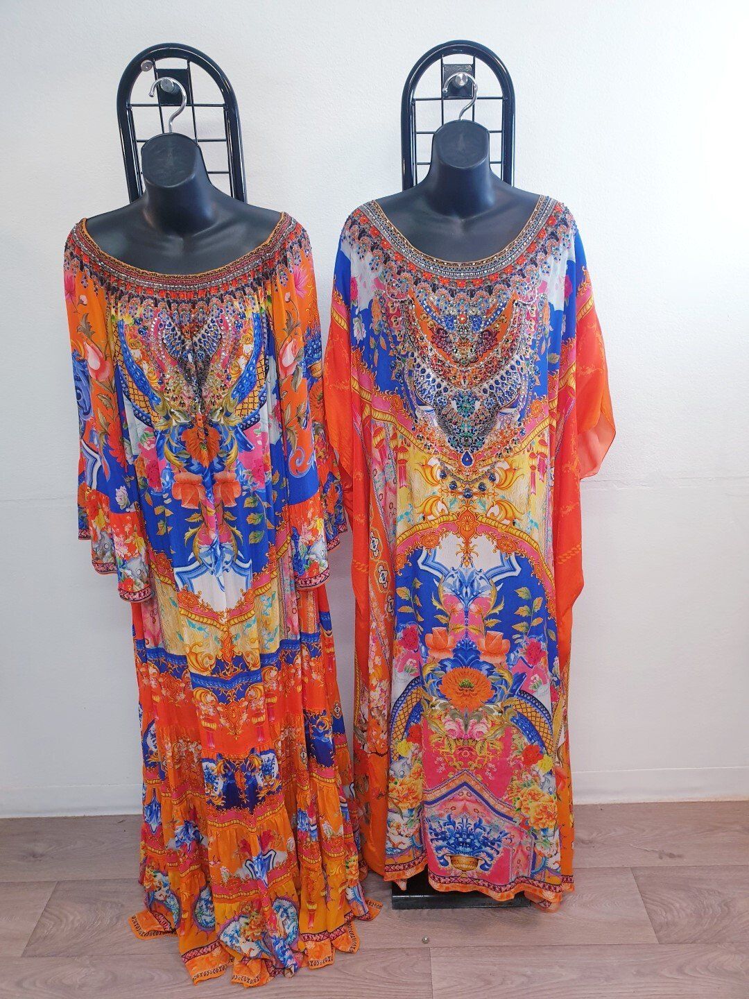 Two ornate, colorful, floor-length kaftans on mannequins. One has long sleeves, the other short.