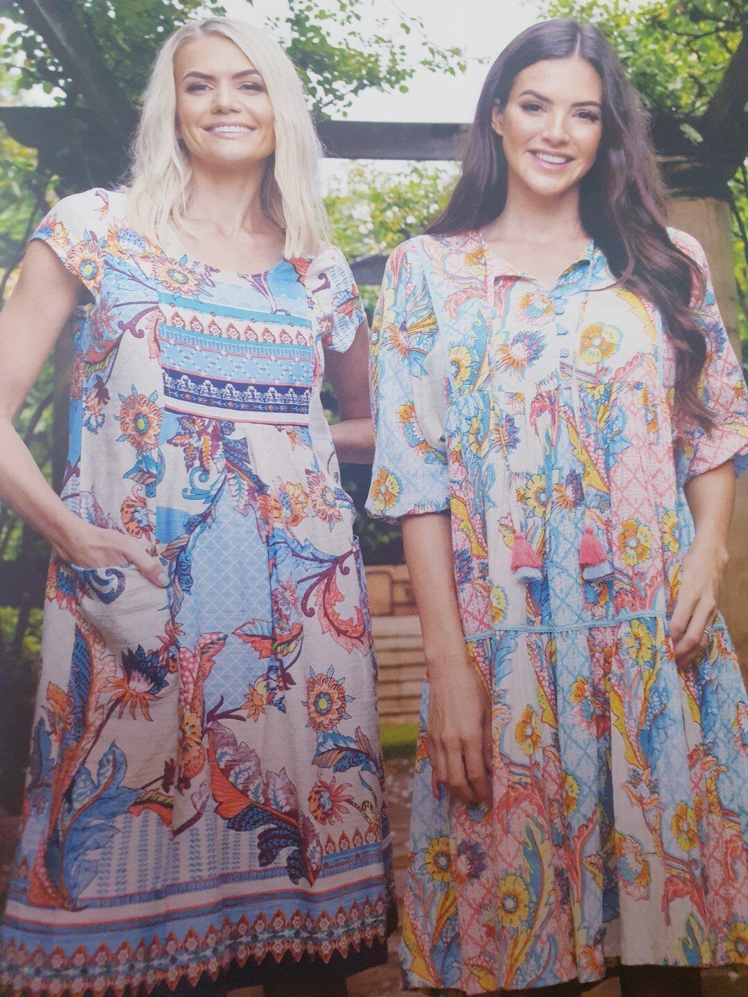 Two women in floral dresses pose outdoors, smiling.