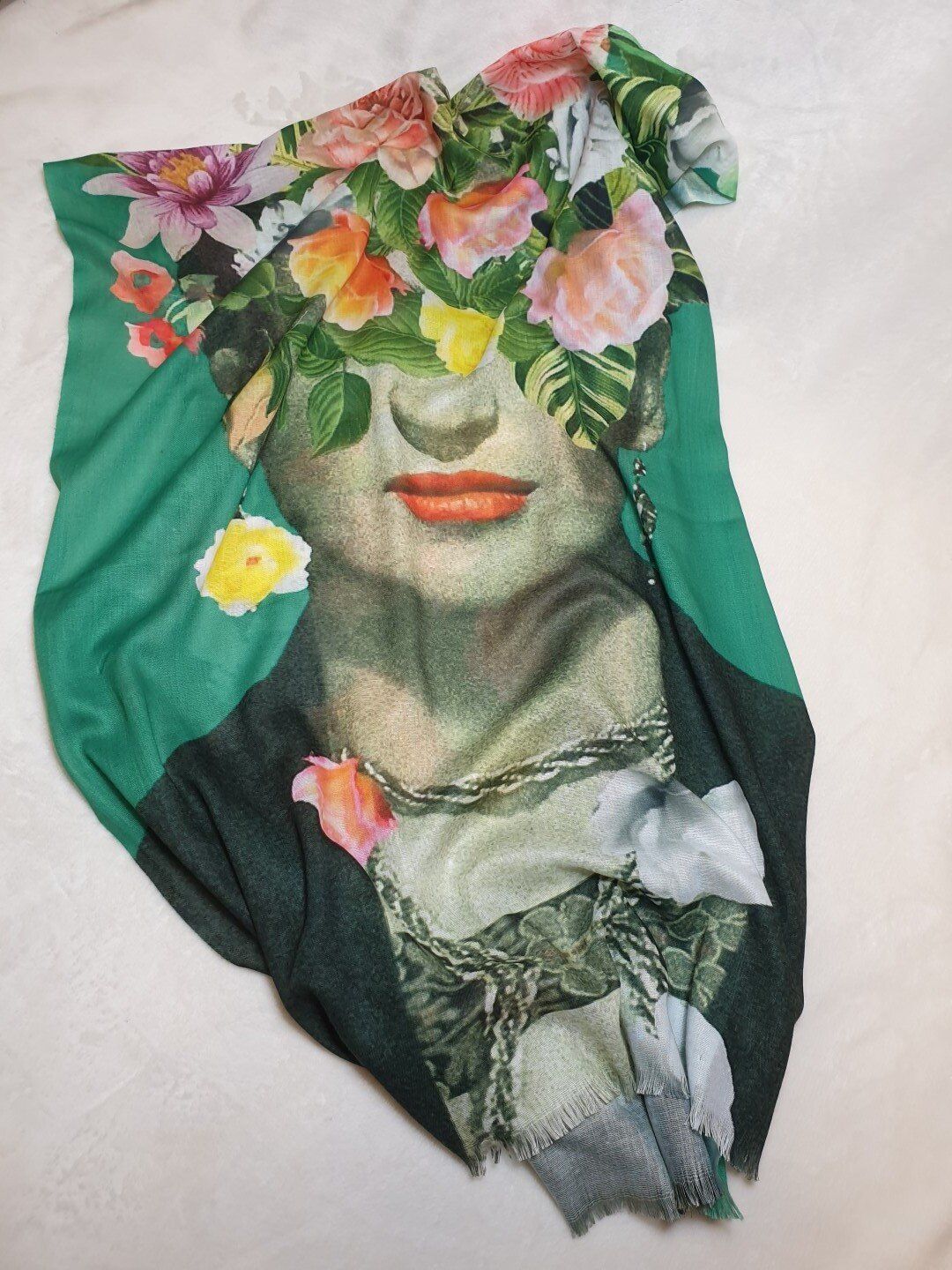 Scarf with a woman's face obscured by colorful flowers, against a green background.
