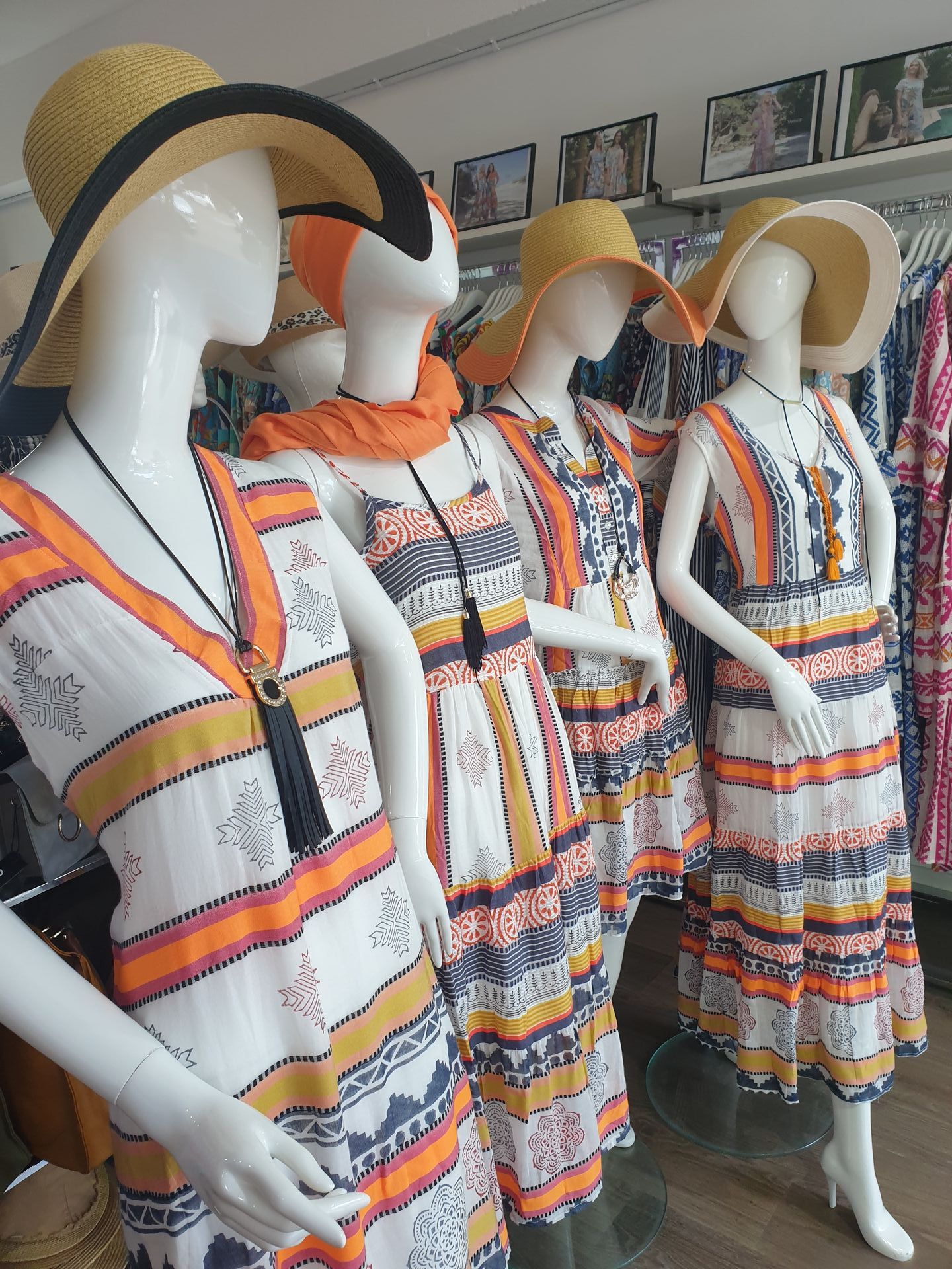 Four mannequins wearing white, orange, and yellow dresses and straw hats in a clothing store.